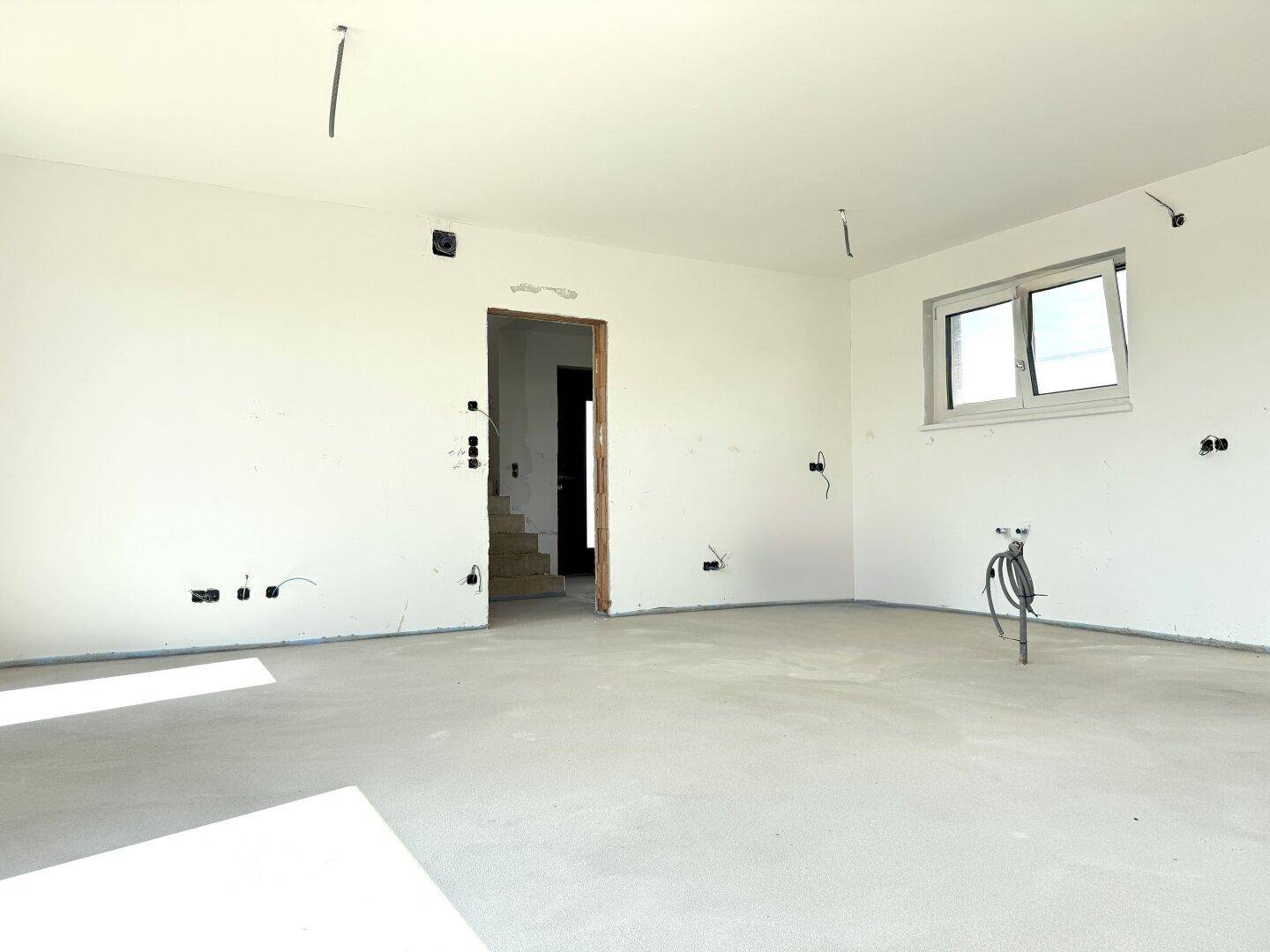 Unfertiger Raum mit Betonboden, weißen Wänden und Fenster, vorbereitet für weitere Installationen.