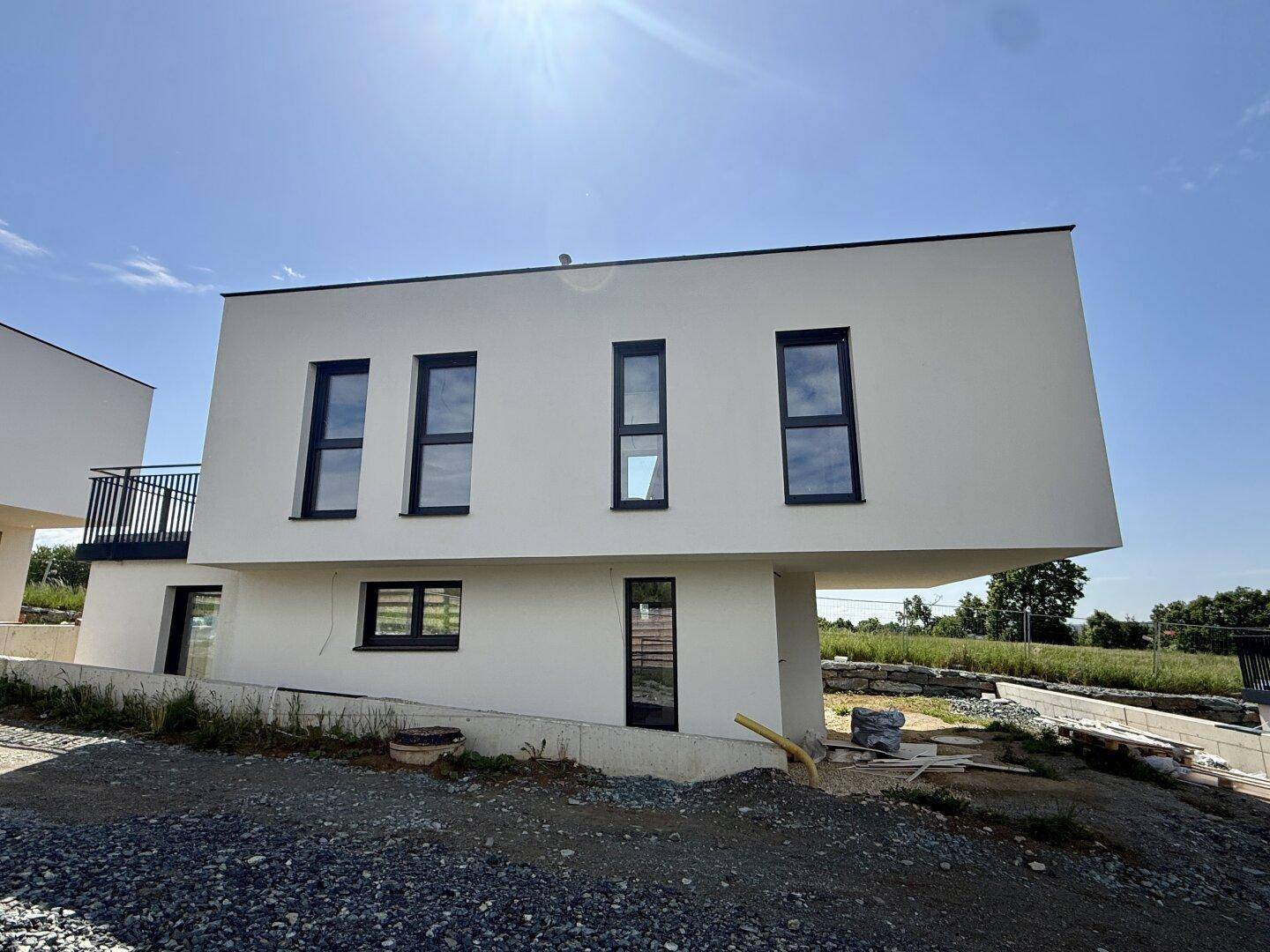 Vorderansicht eines modernen weißen Hauses mit Flachdach und dunklen Fenstern, im Bau.
