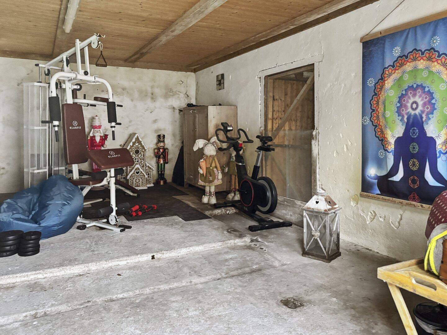 Fitnessraum mit verschiedenen Trainingsgeräten und einem Meditationsbild an der rustikalen Wand.