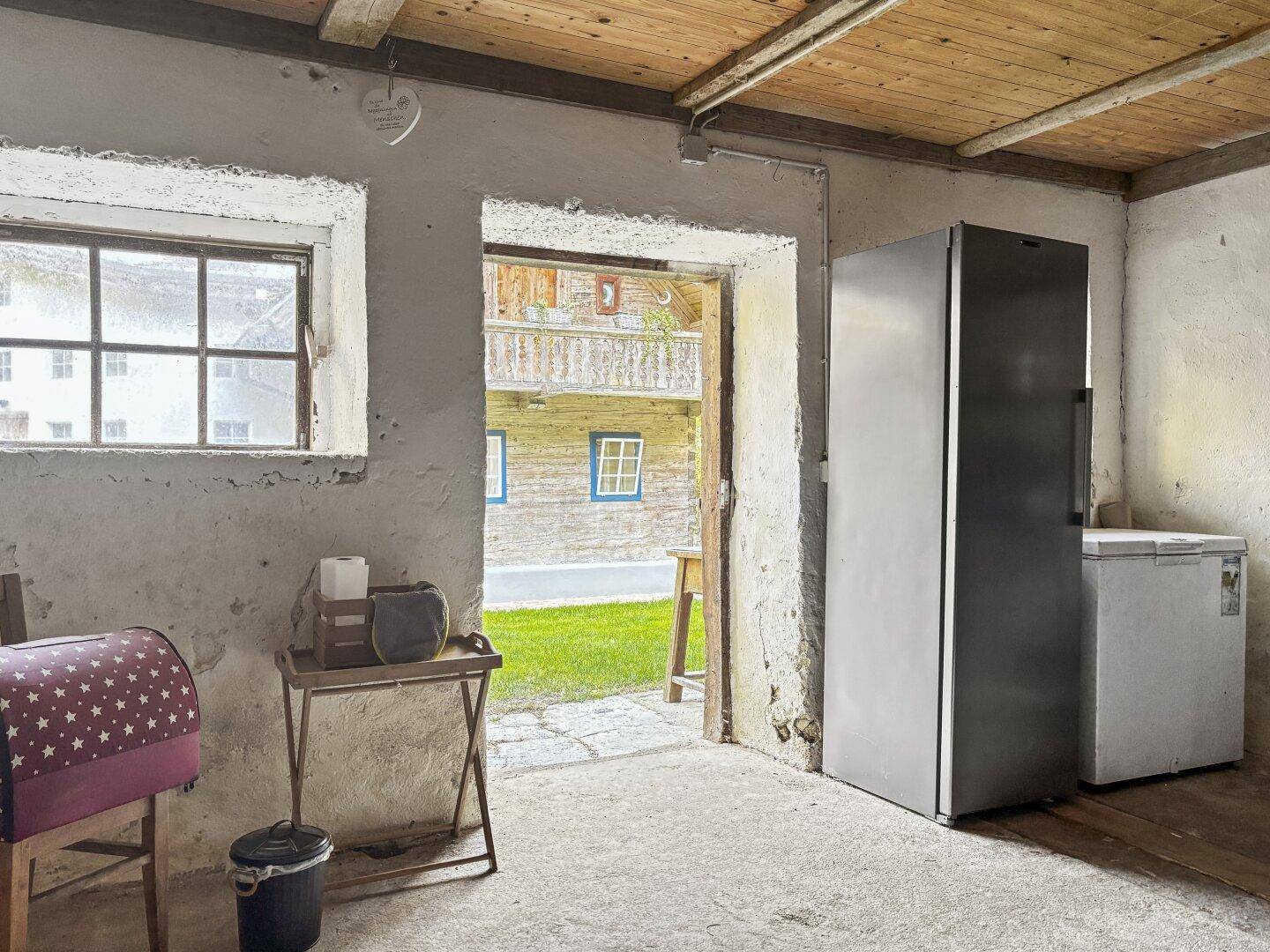 Einfacher Abstellraum mit Kühlschrank und Gefriertruhe, Blick nach draußen durch die Türöffnung.