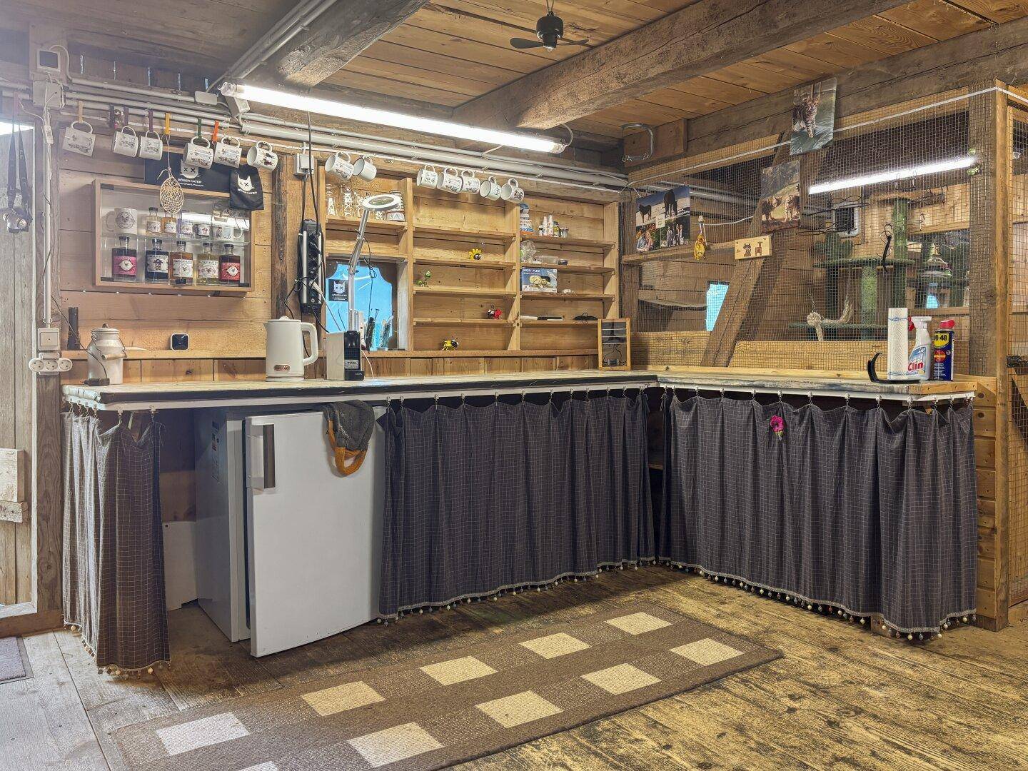Einfache Küchenzeile mit Vorhängen und Kühlschrank in einem rustikalen Raum mit Holzböden.