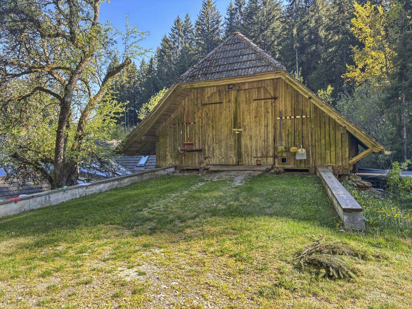 Rustikale Holzscheune mit Werkzeugen an der Fassade, umgeben von einer grünen Wiese.