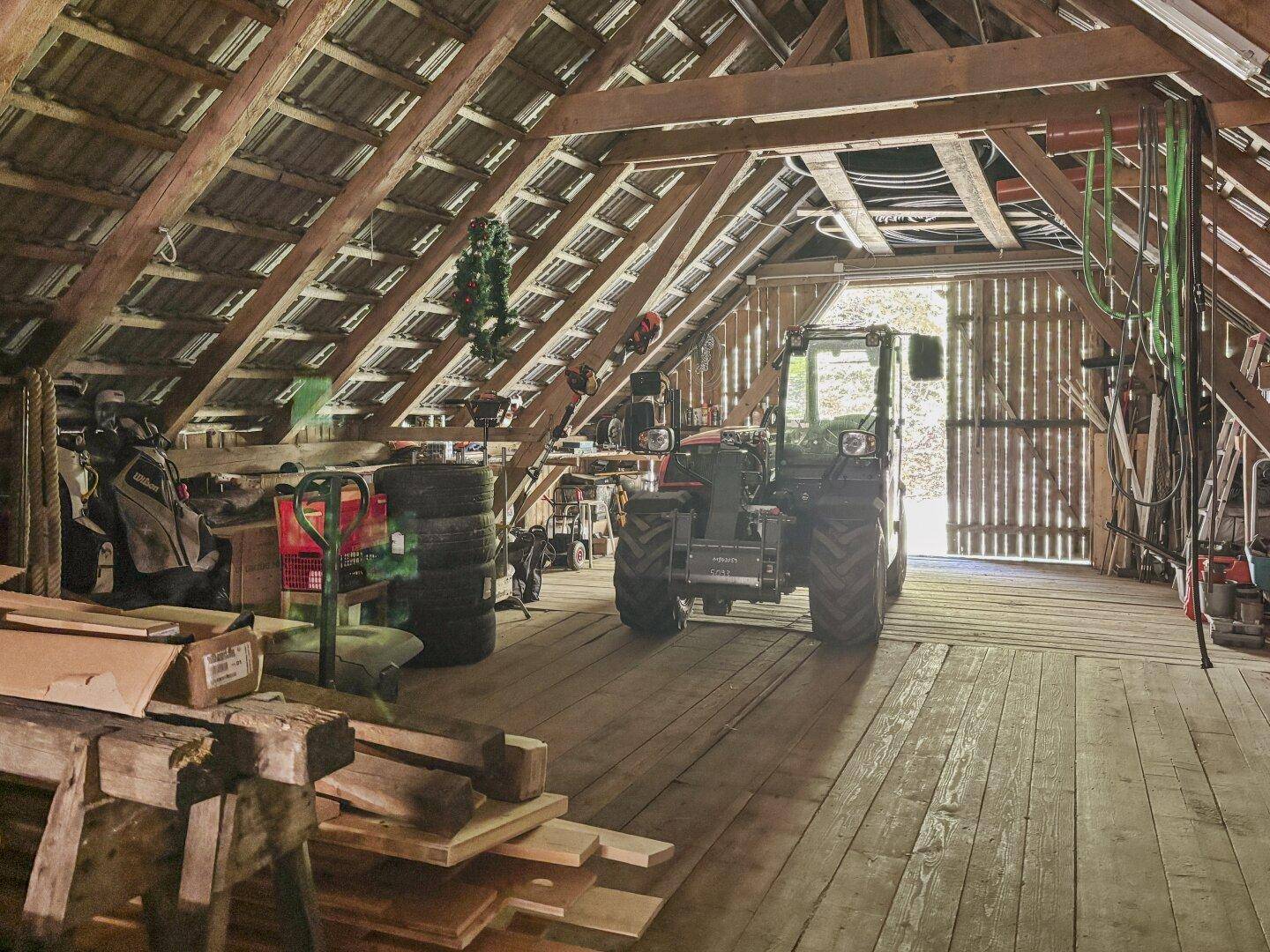 Großer Dachboden mit Holzbalken und -boden, dient als Abstellfläche für landwirtschaftliche Geräte.