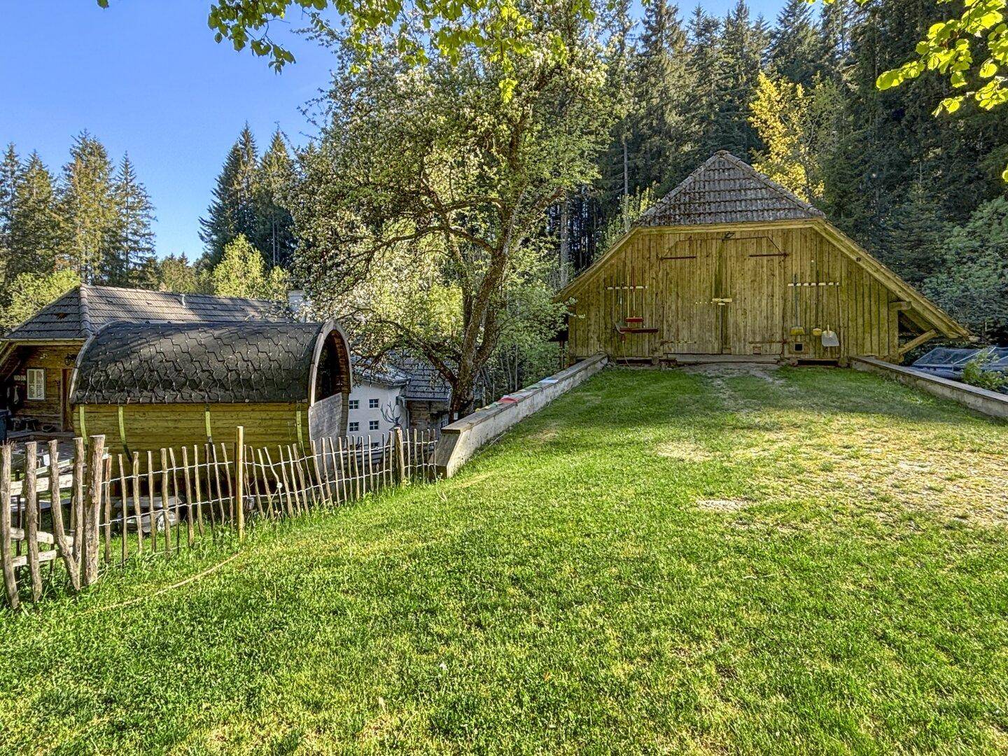 Rustikales Scheunengebäude und ein kleineres Holzhaus, umgeben von einer gepflegten Rasenfläche.