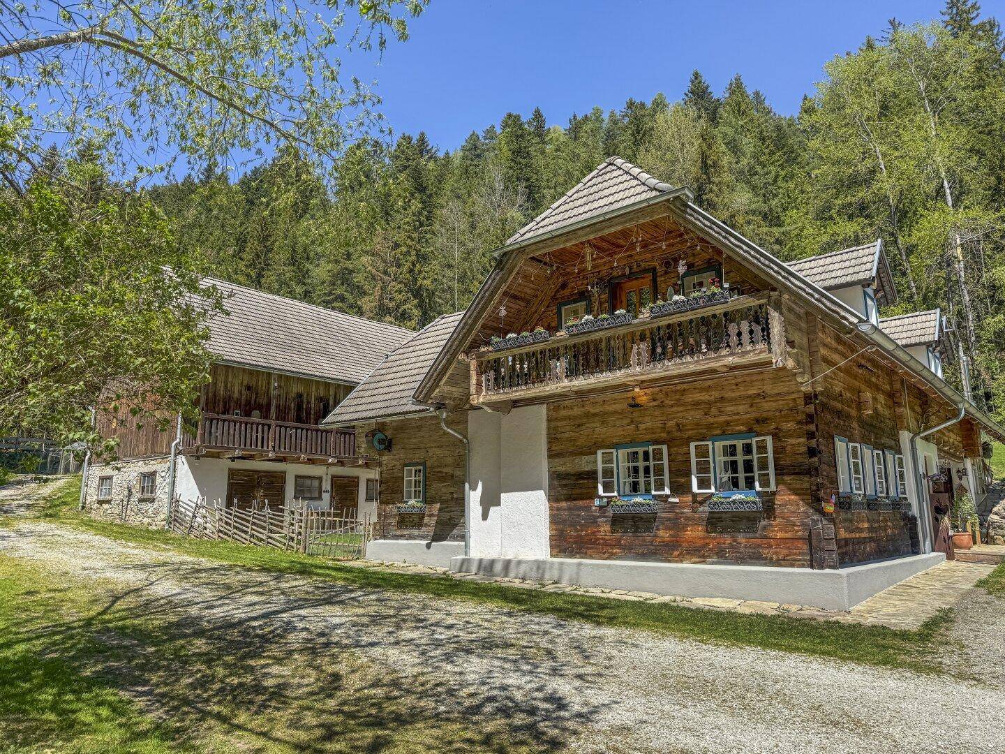 Charmantes Holzhaus mit traditionellem Balkon und Satteldach, eingebettet in eine grüne Landschaft.