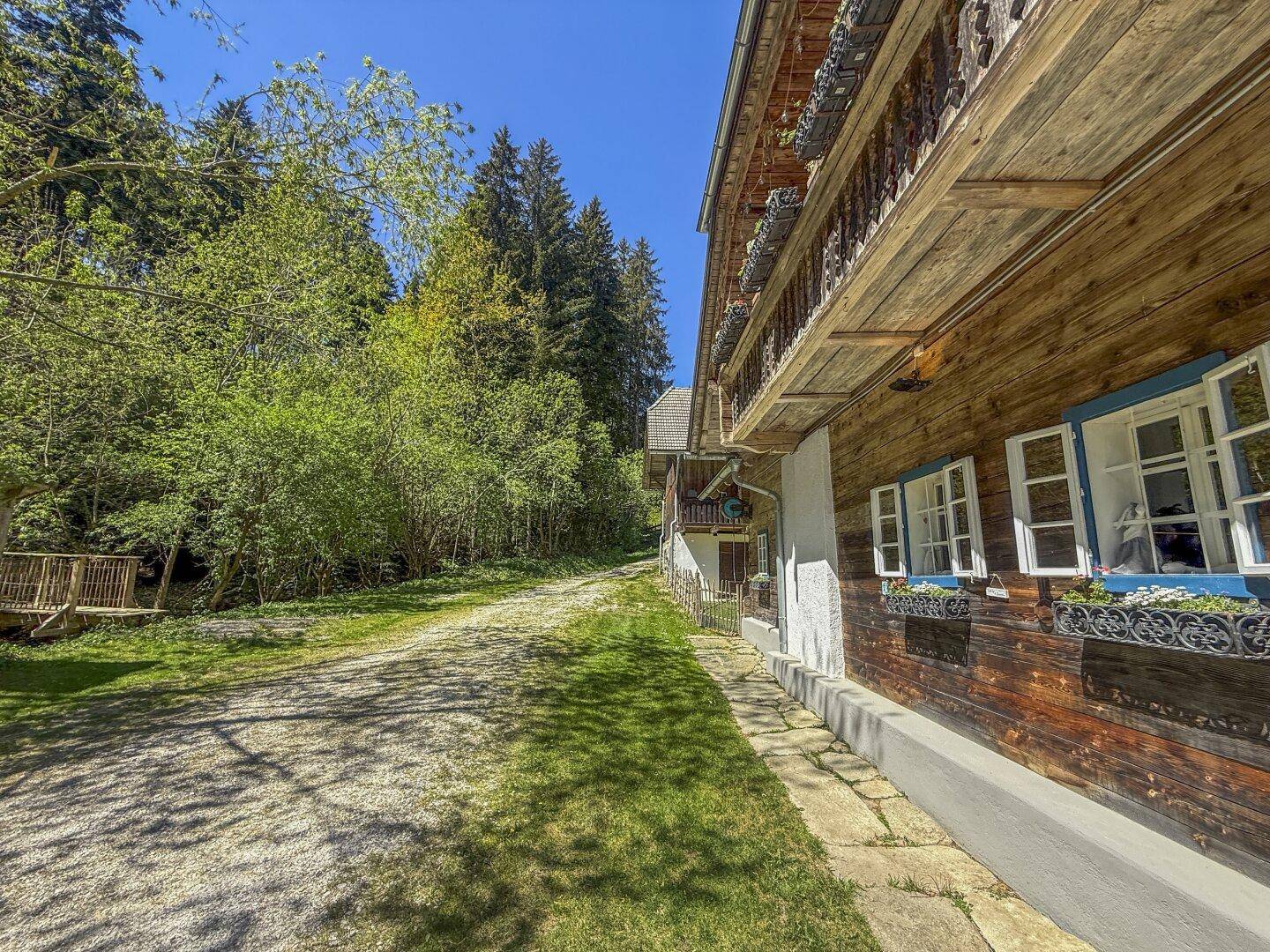 Seitenansicht eines traditionellen Holzhauses mit blauen Fensterläden und Blumenkästen.