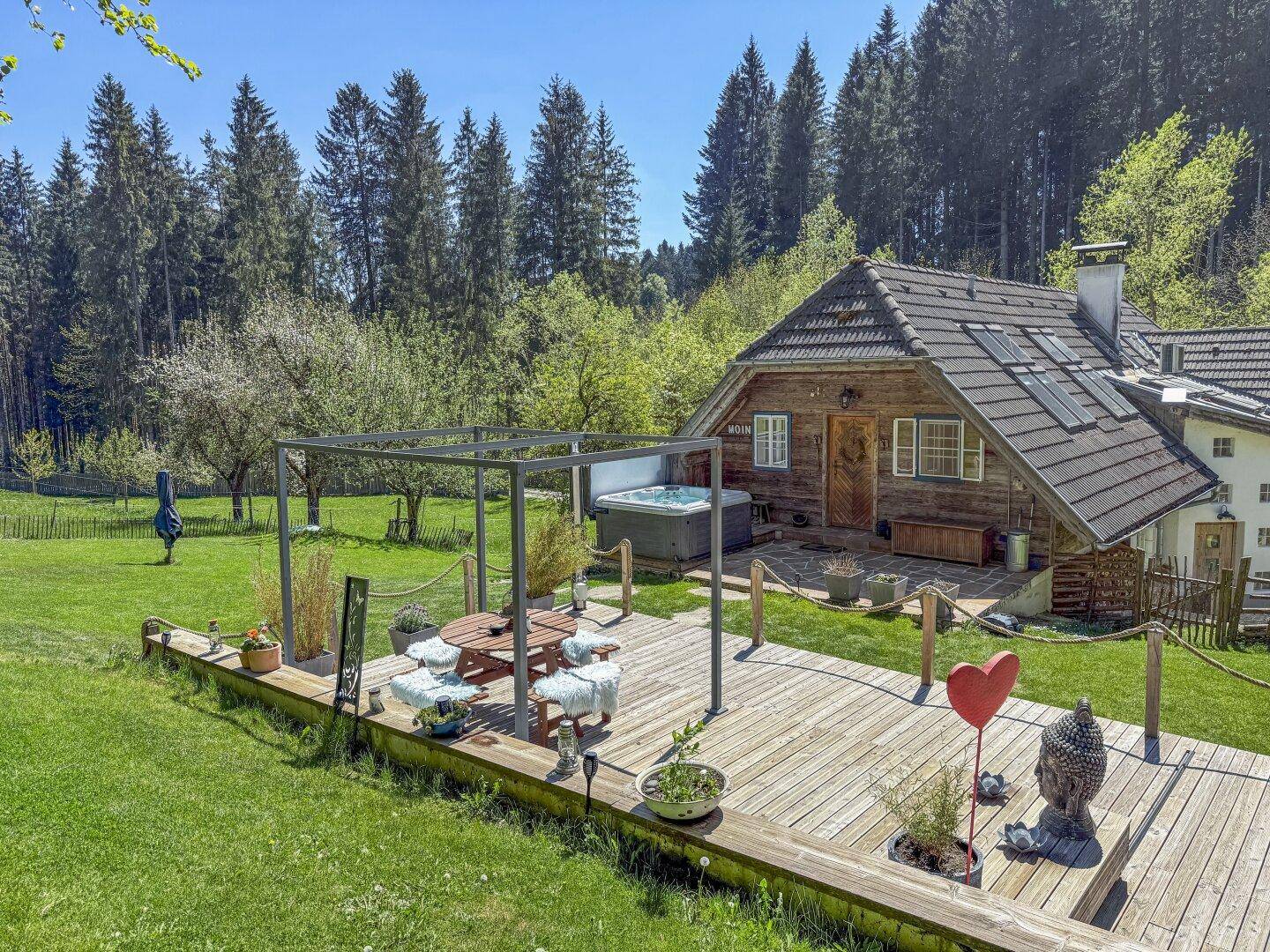 Große Holzterrasse mit Essbereich im Freien, Whirlpool und weitem Blick auf die grüne Landschaft.