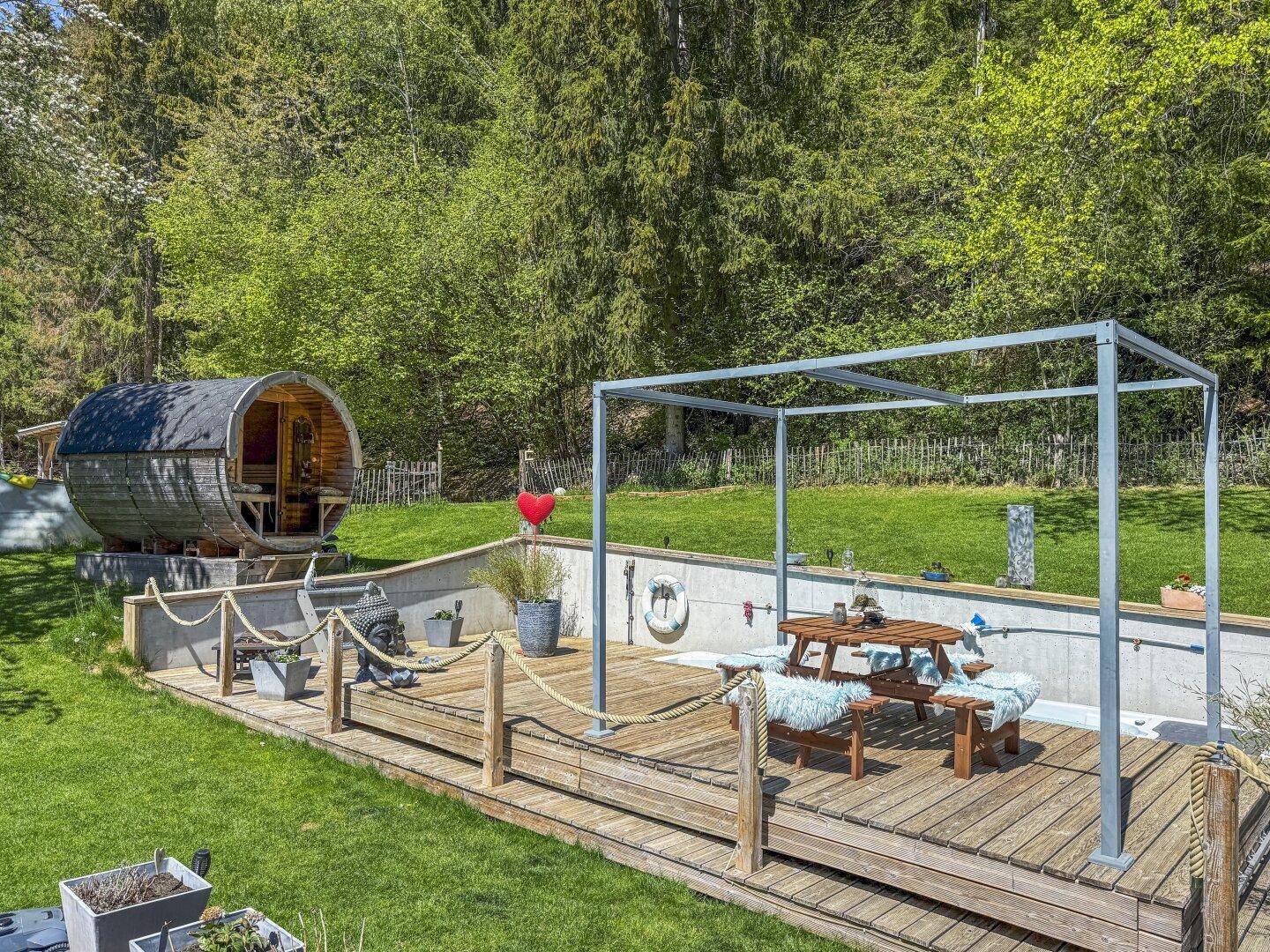 Außenbereich mit Holzterrasse, Esstisch und einer Fasssauna im Grünen.