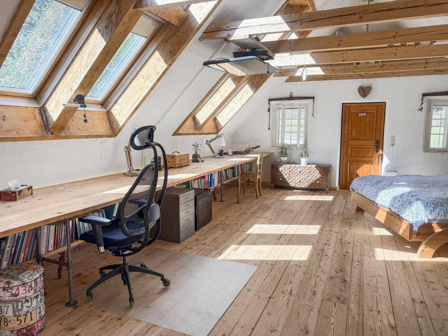 Helles Schlafzimmer im Dachgeschoss mit großem Schreibtisch, Holzboden und Dachfenstern.
