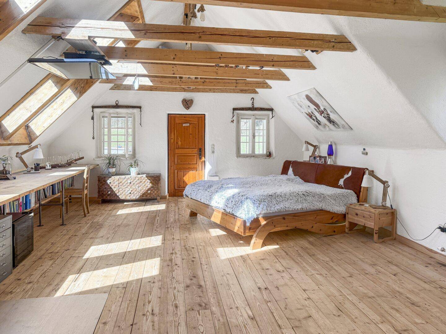 Geräumiges Schlafzimmer im Dachgeschoss mit Holzboden, Doppelbett und großem Schreibtisch.