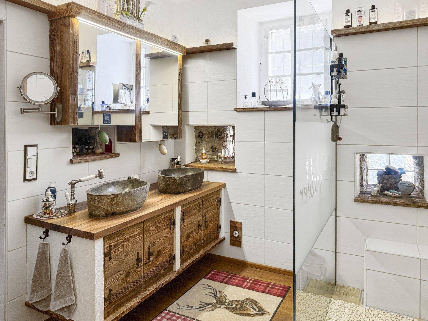 Modernes Badezimmer mit Doppelwaschbecken aus Stein, Holzunterschrank und begehbarer Dusche.