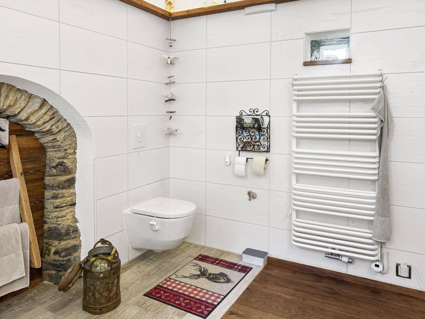 Separates WC mit wandhängender Toilette, beheiztem Handtuchhalter und rustikalen Akzenten.