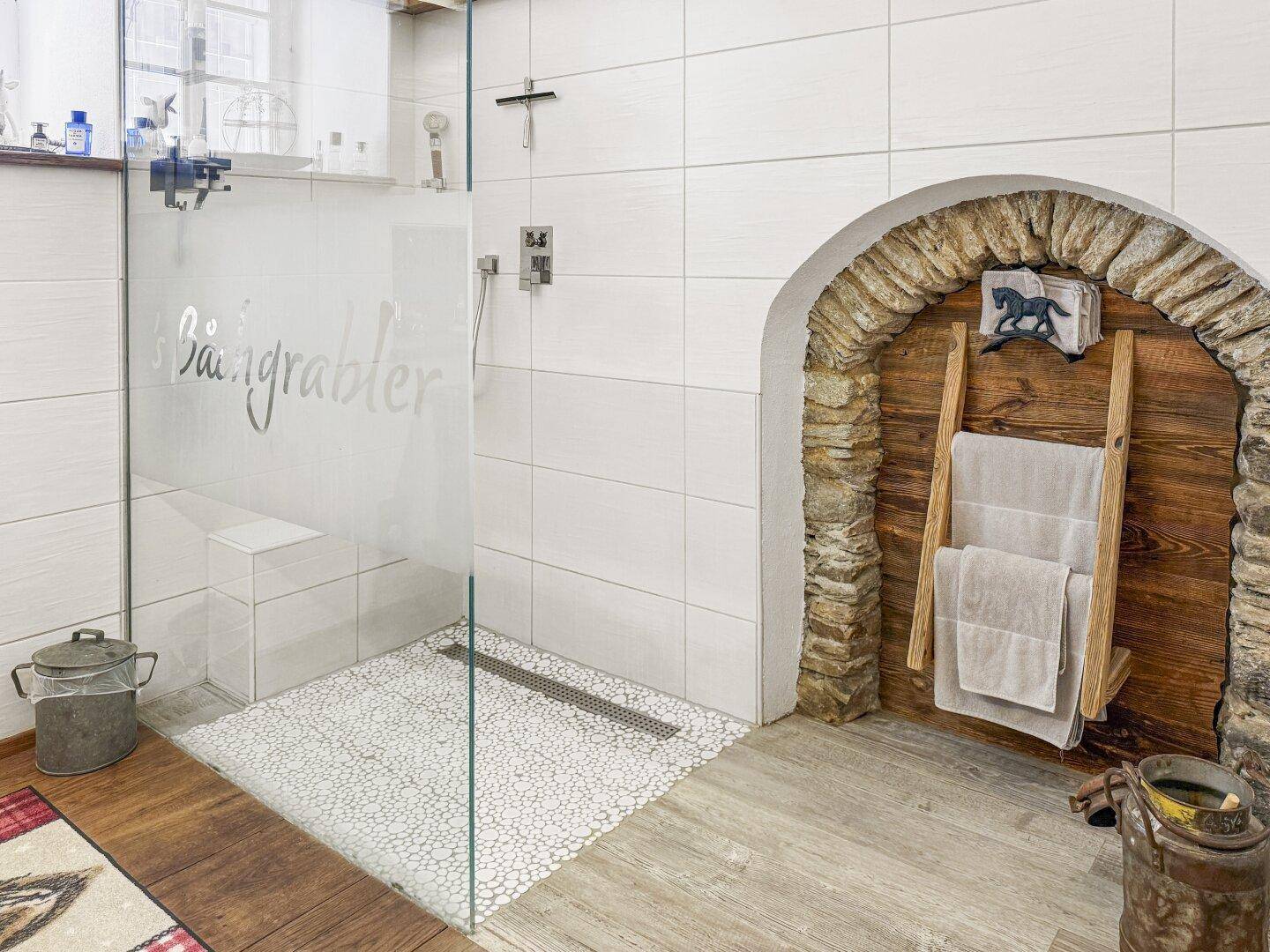 Geräumige begehbare Dusche mit Glaswand und Mosaikboden, ergänzt durch rustikale Holzelemente.