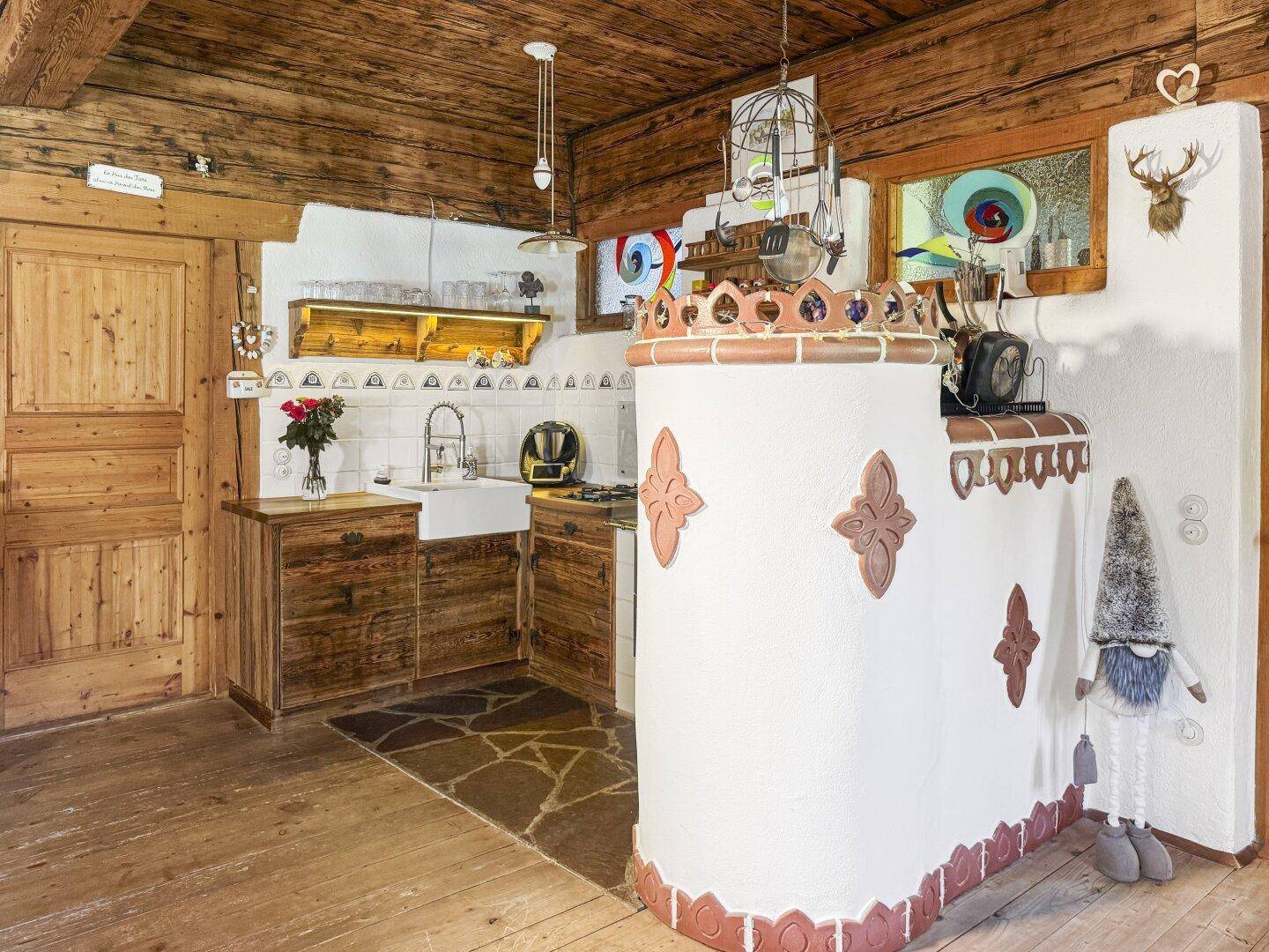 Gemütliche Küche im Landhausstil mit Kachelofen, Holzbalkendecke und rustikalen Möbeln.