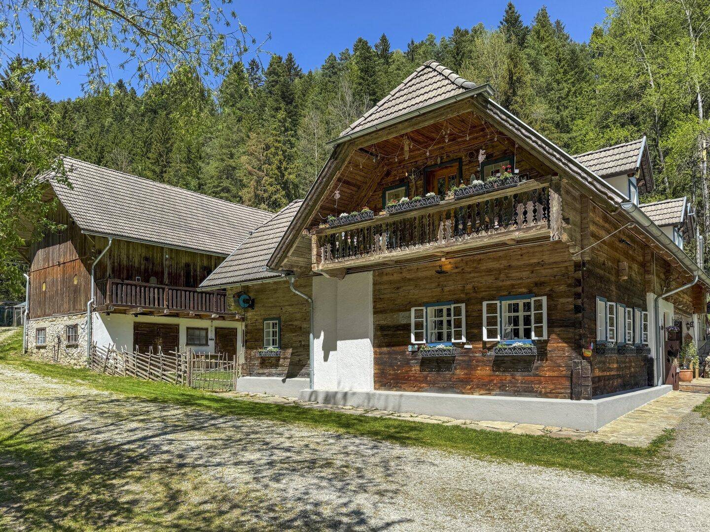 Traditionelles Holzhaus mit Satteldach und einem Nebengebäude, umgeben von viel Grün.
