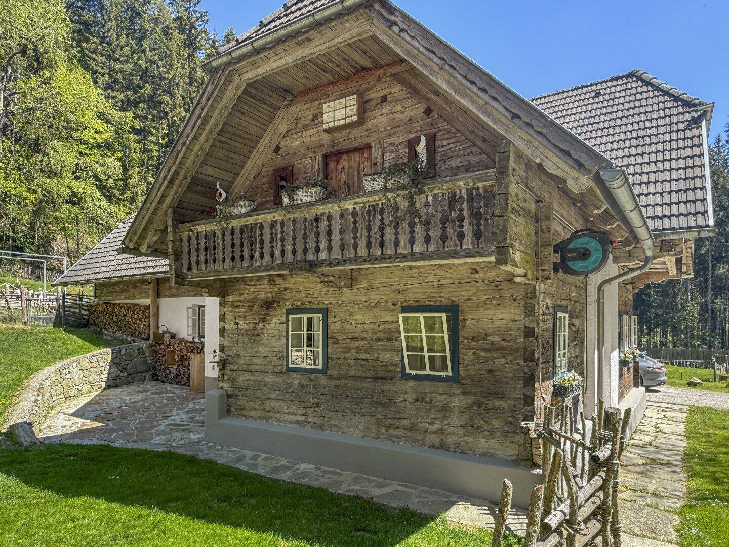 Charmantes Holzhaus mit traditionellem Balkon, grüner Umgebung und Blick auf den Wald.