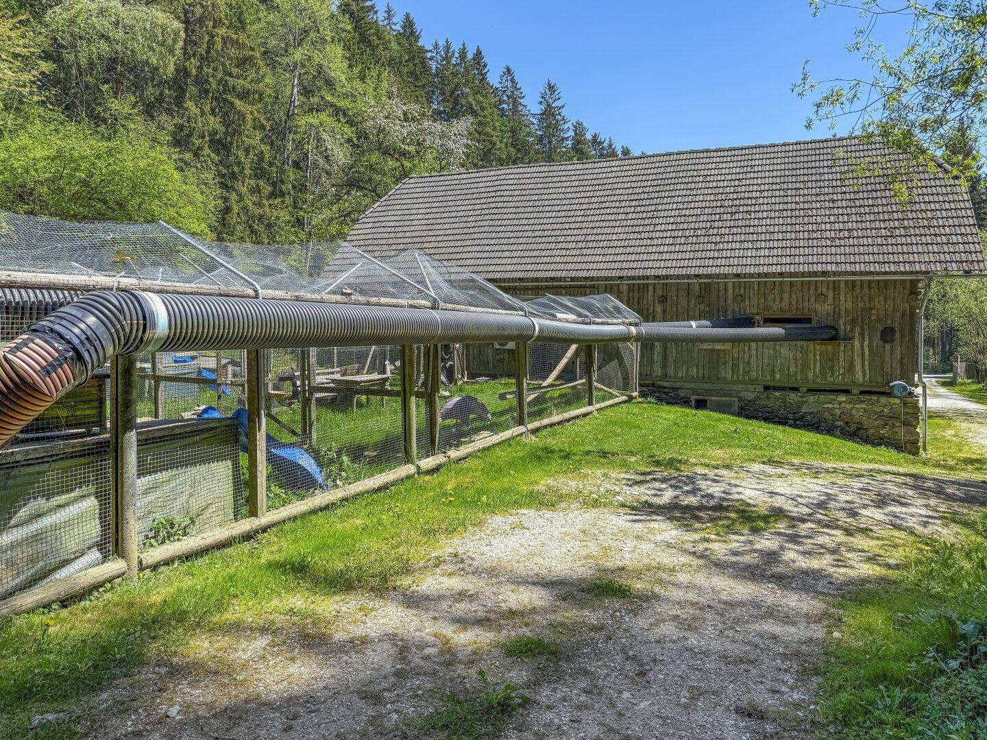 Außengebäude aus Holz mit einem Rohrsystem, das zu einem umzäunten Bereich führt.