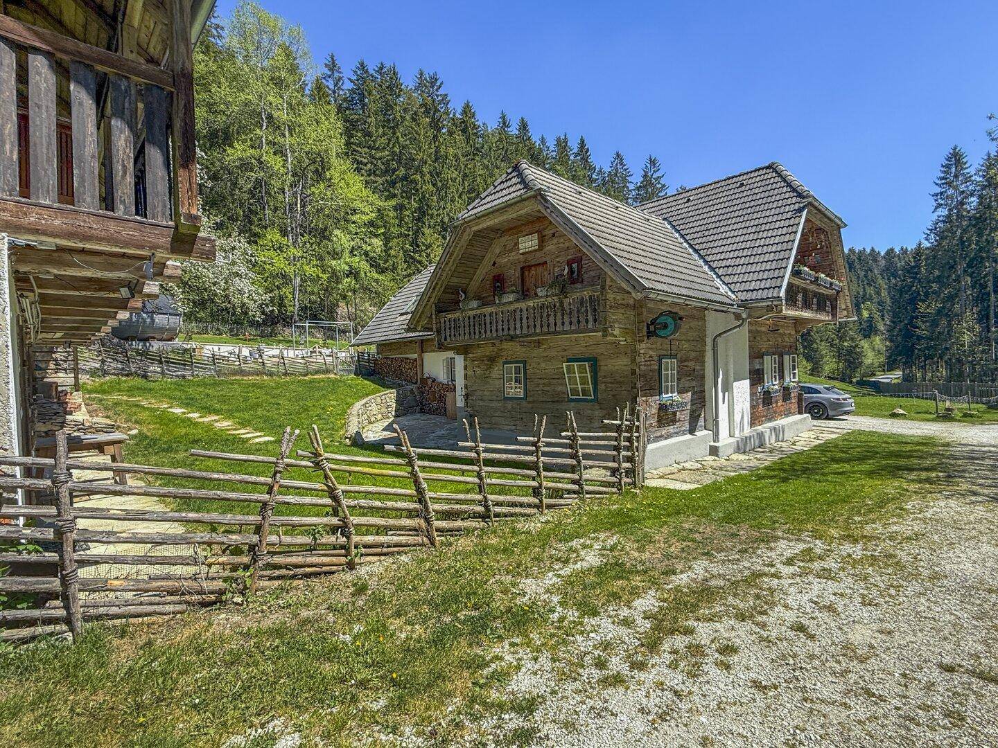 Vorderansicht eines traditionellen Holzhauses mit Kiesauffahrt und weitläufigem Rasenbereich.