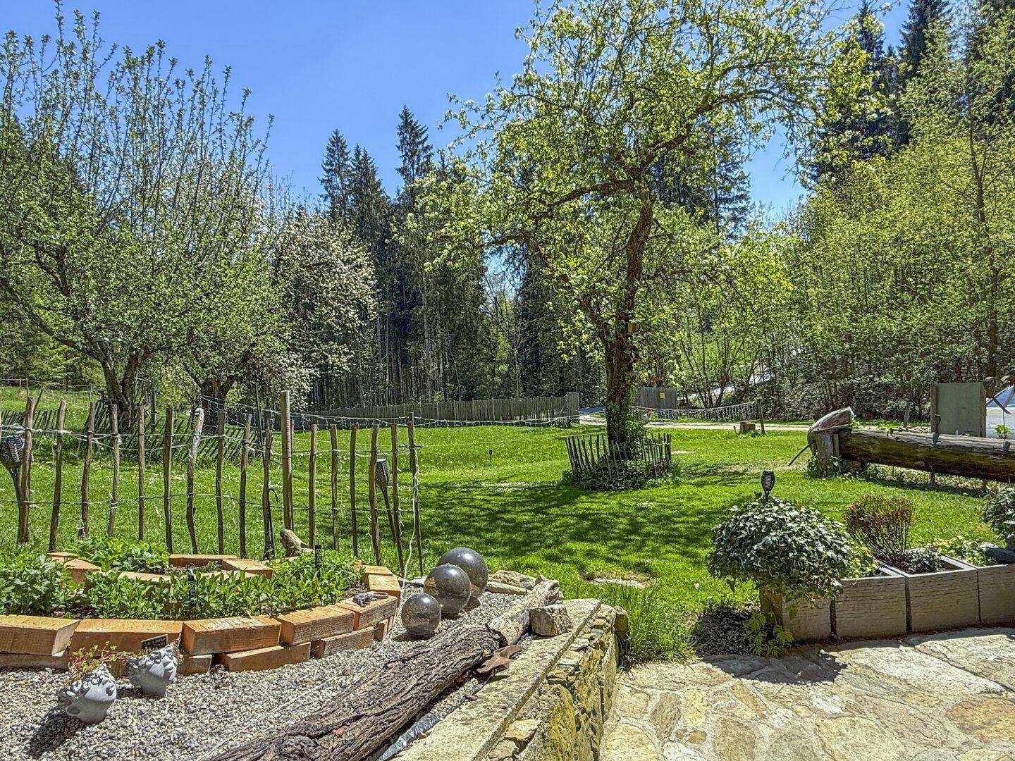 Idyllischer Gartenbereich mit Rasenfläche, Hochbeeten und Bäumen, umgeben von ländlicher Natur.