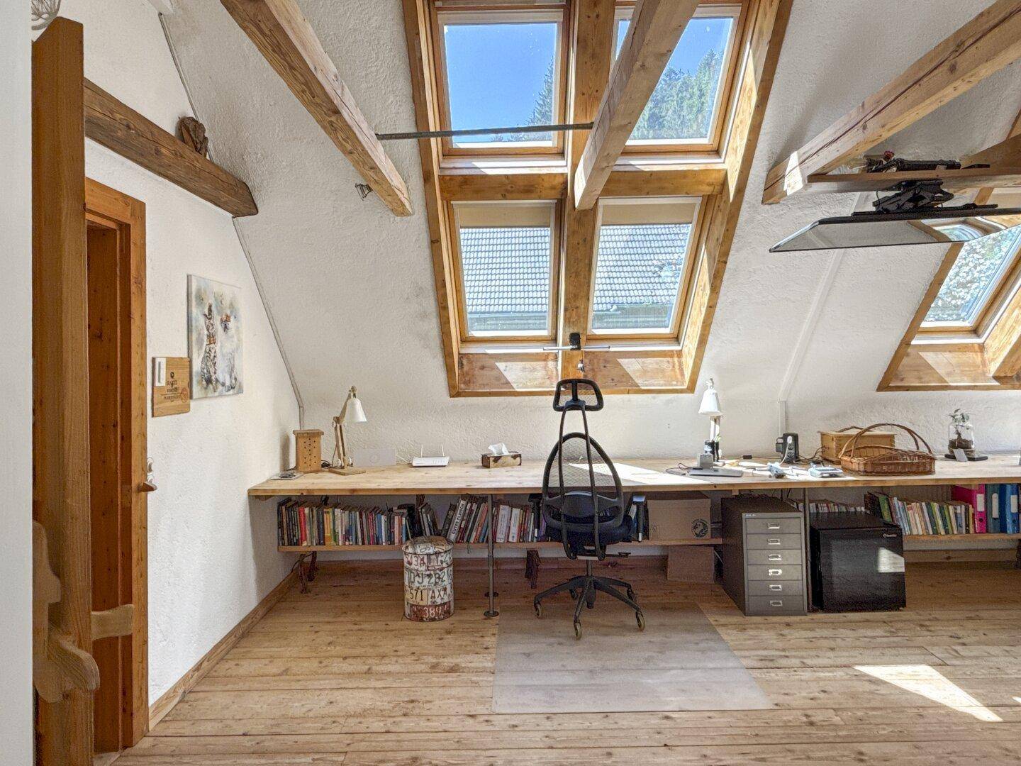 Geräumiges Dachzimmer mit Holzboden, vielen Dachfenstern und einem langen Schreibtisch unter den Schrägen.