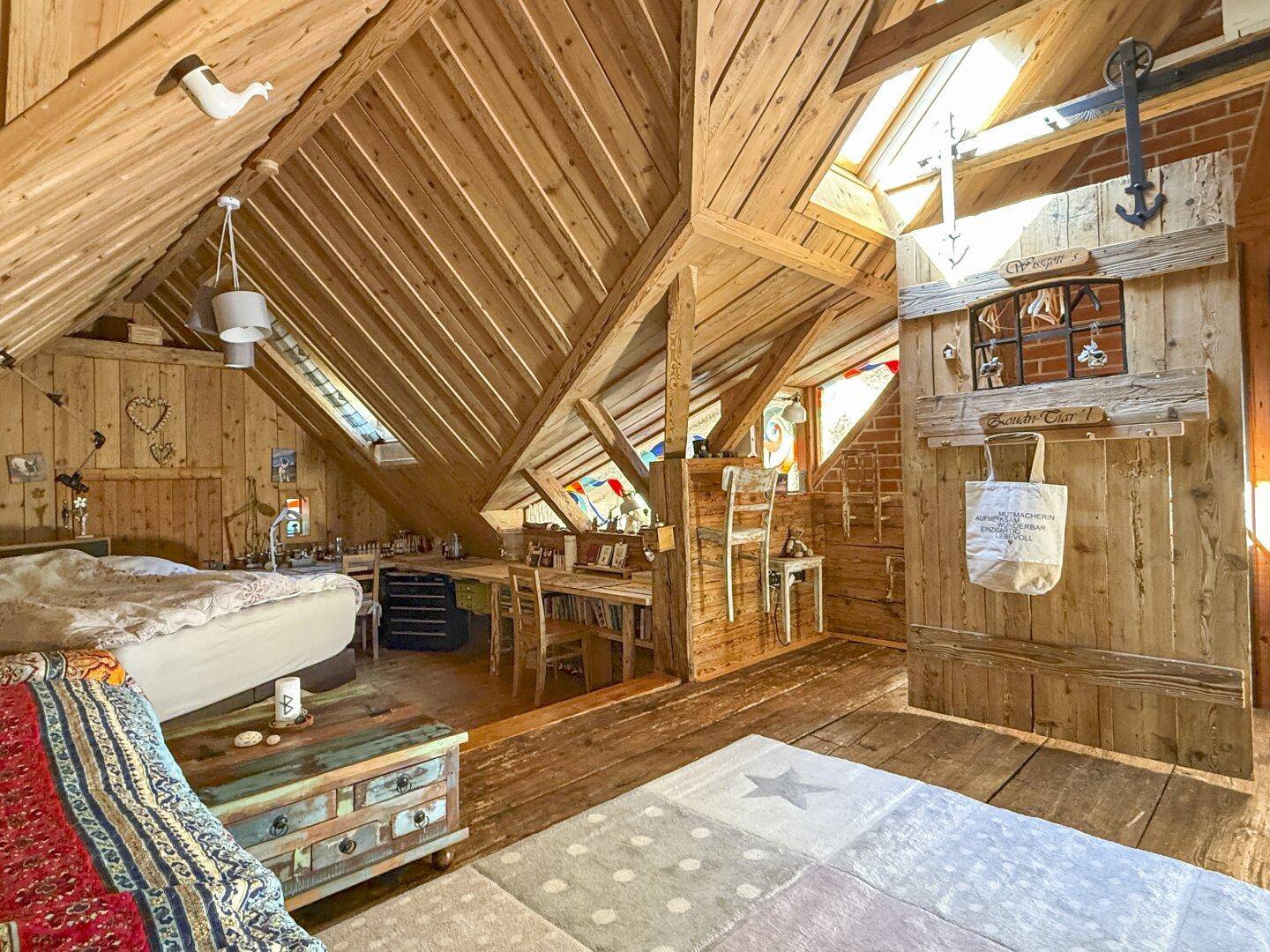 Gemütliches Dachzimmer mit viel Holz, schrägen Wänden, bunten Dekorationen und einem Arbeitsbereich.