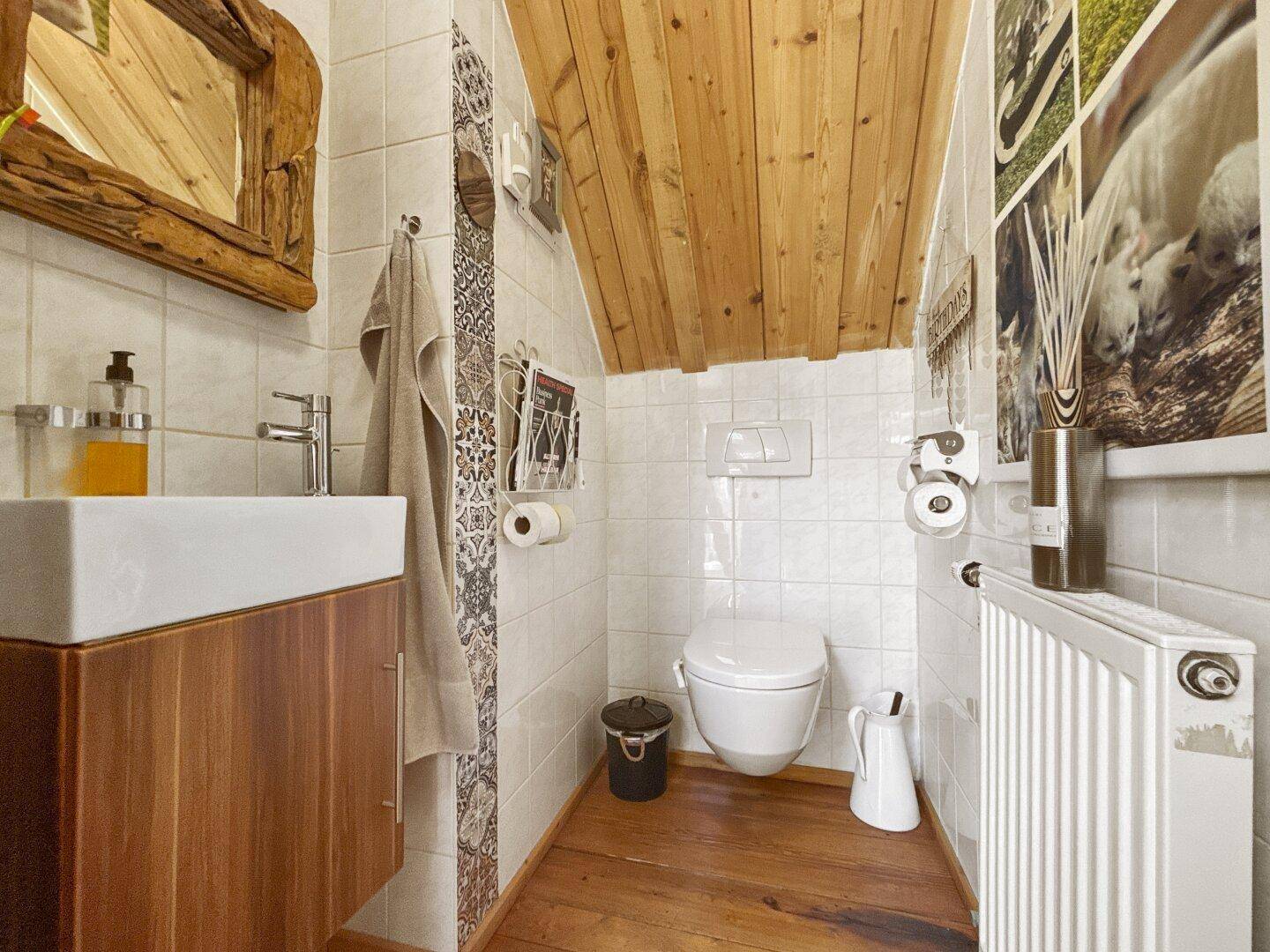 Helles Gäste-WC mit weißen Fliesen, Holzdecke, Holzboden und wandhängendem WC.