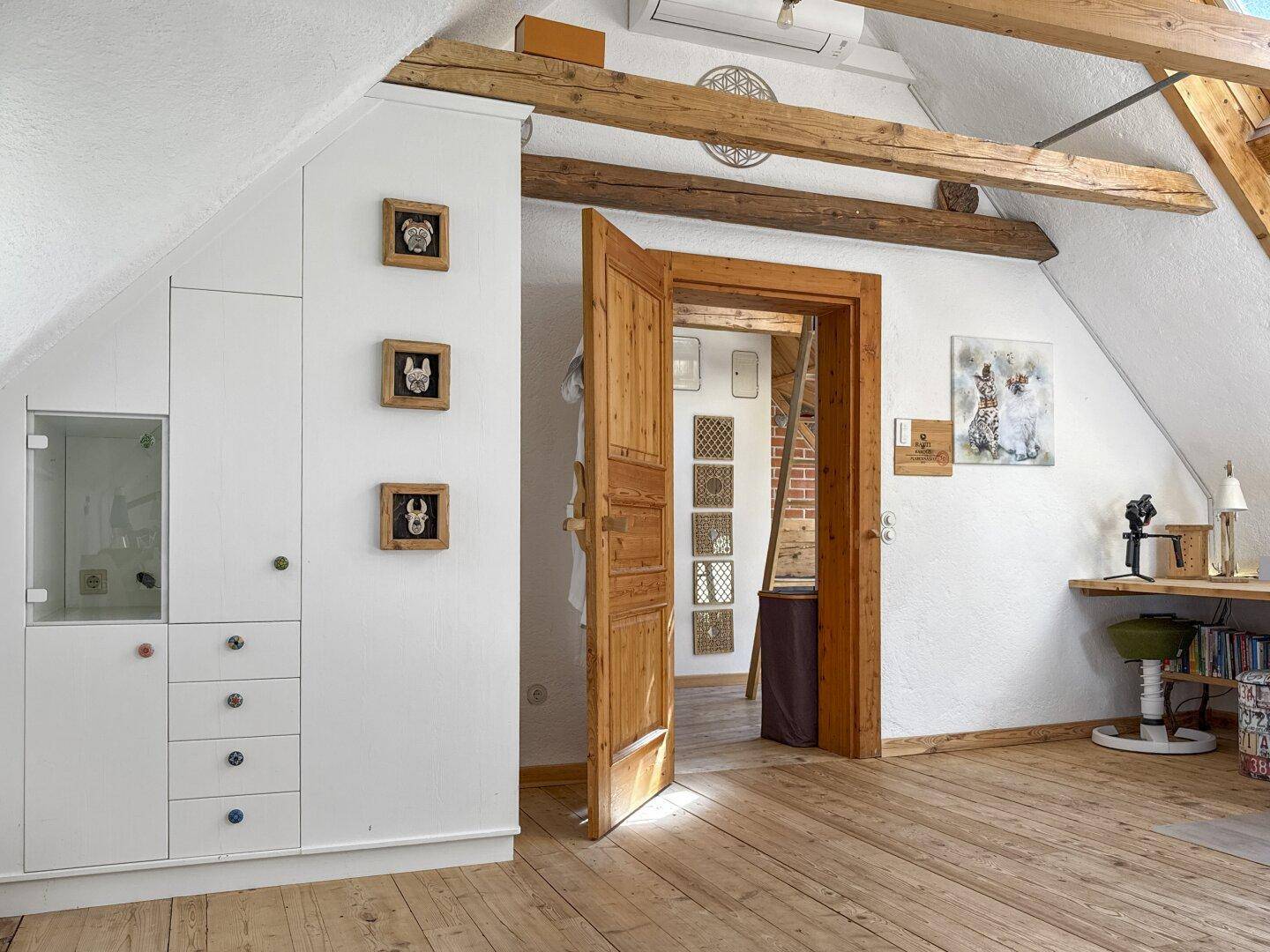 Heller Dachraum mit Einbauschränken, Holzboden und einer Holztür, die zu einem weiteren Bereich führt.