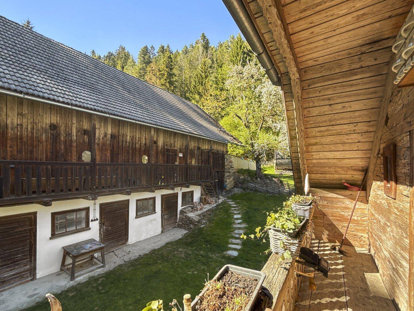 Seitenansicht des Holzhauses mit Blick auf den Garten und einen weiteren Gebäudeteil.