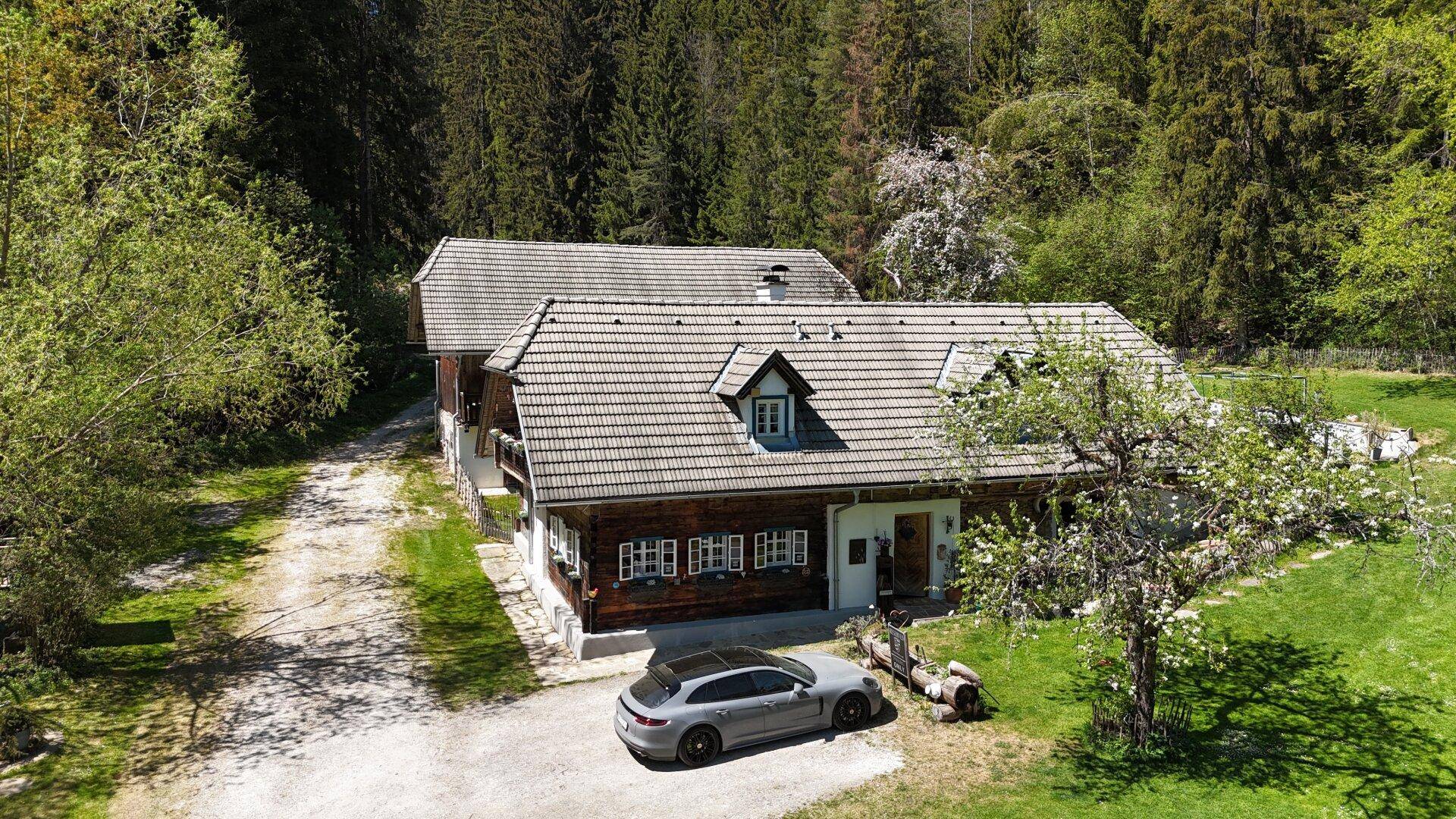 Luftaufnahme eines traditionellen Hauses mit geparktem Auto, umgeben von Rasen und Bäumen.