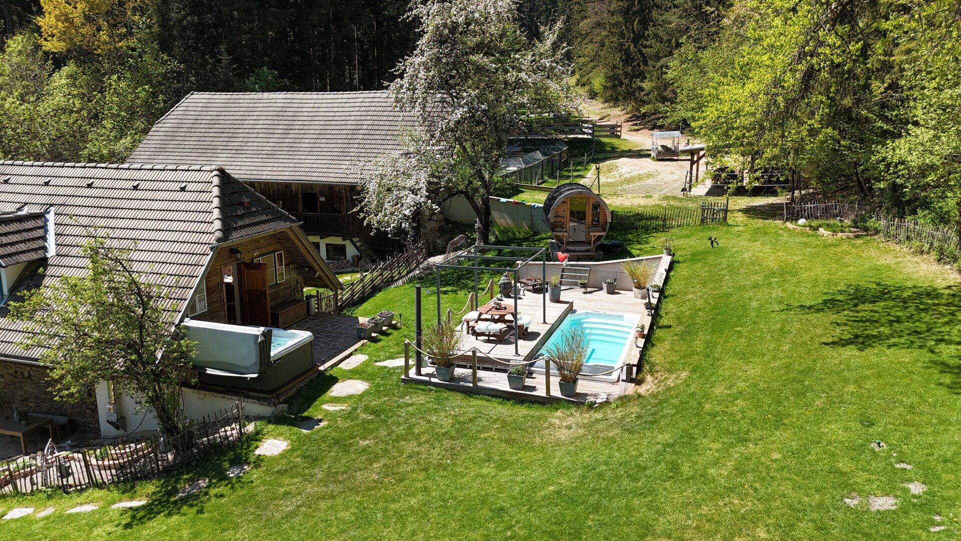 Weitläufige Außenansicht des Anwesens mit Pool, Whirlpool und Fasssauna, umgeben von Wald.