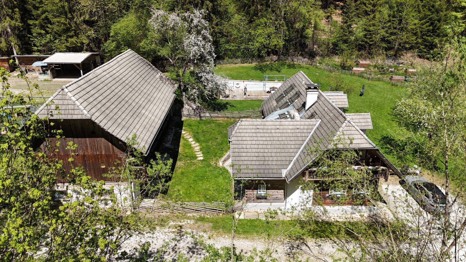 Luftaufnahme des Anwesens mit mehreren rustikalen Gebäuden und weitläufigen Grünflächen im Wald.