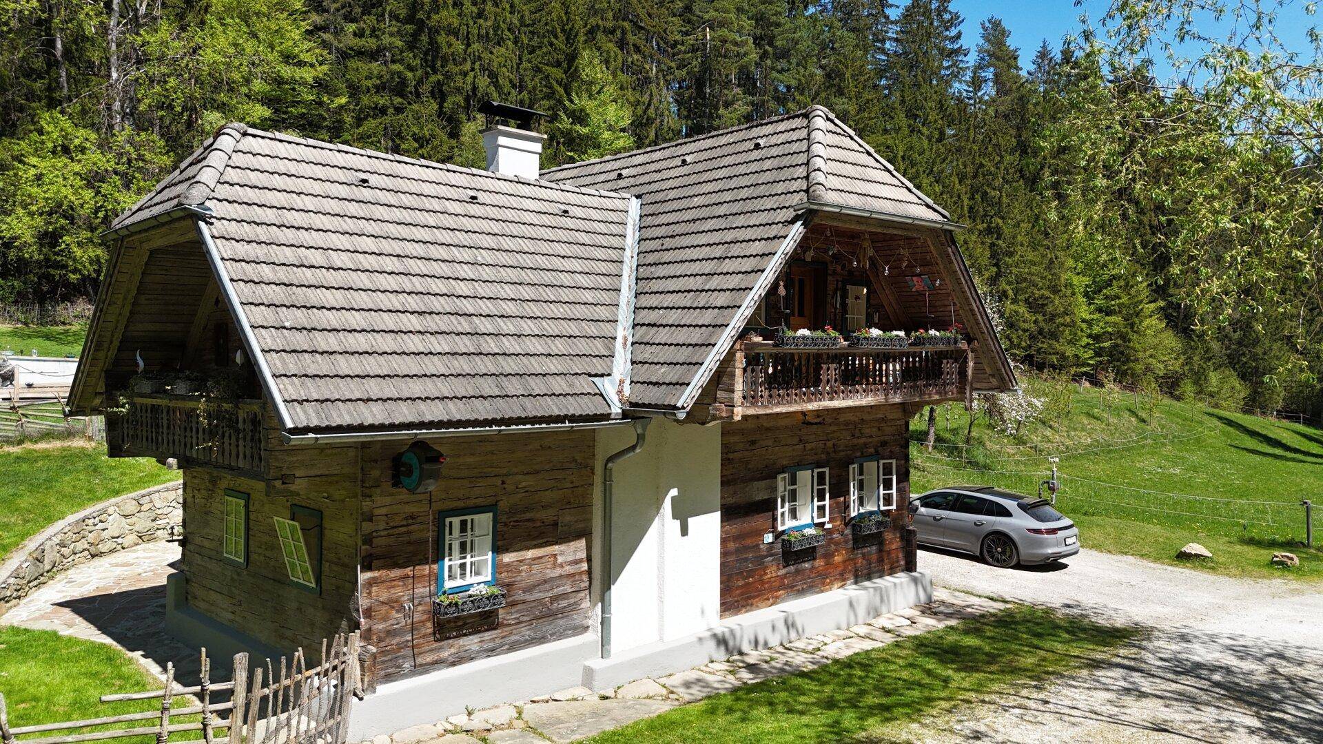 Charmantes Holzhaus mit traditionellem Balkon und Satteldach, umgeben von üppiger Natur.