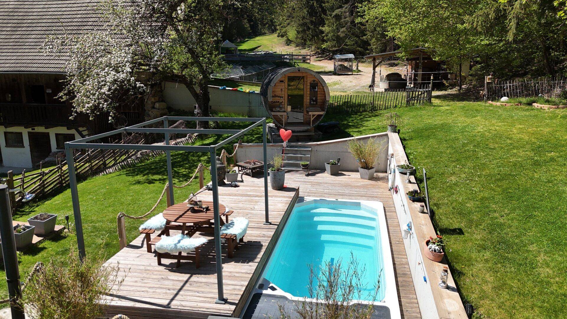 Vogelperspektive des weitläufigen Gartens mit Pool, Holzterrasse, Fasssauna und viel Rasenfläche.
