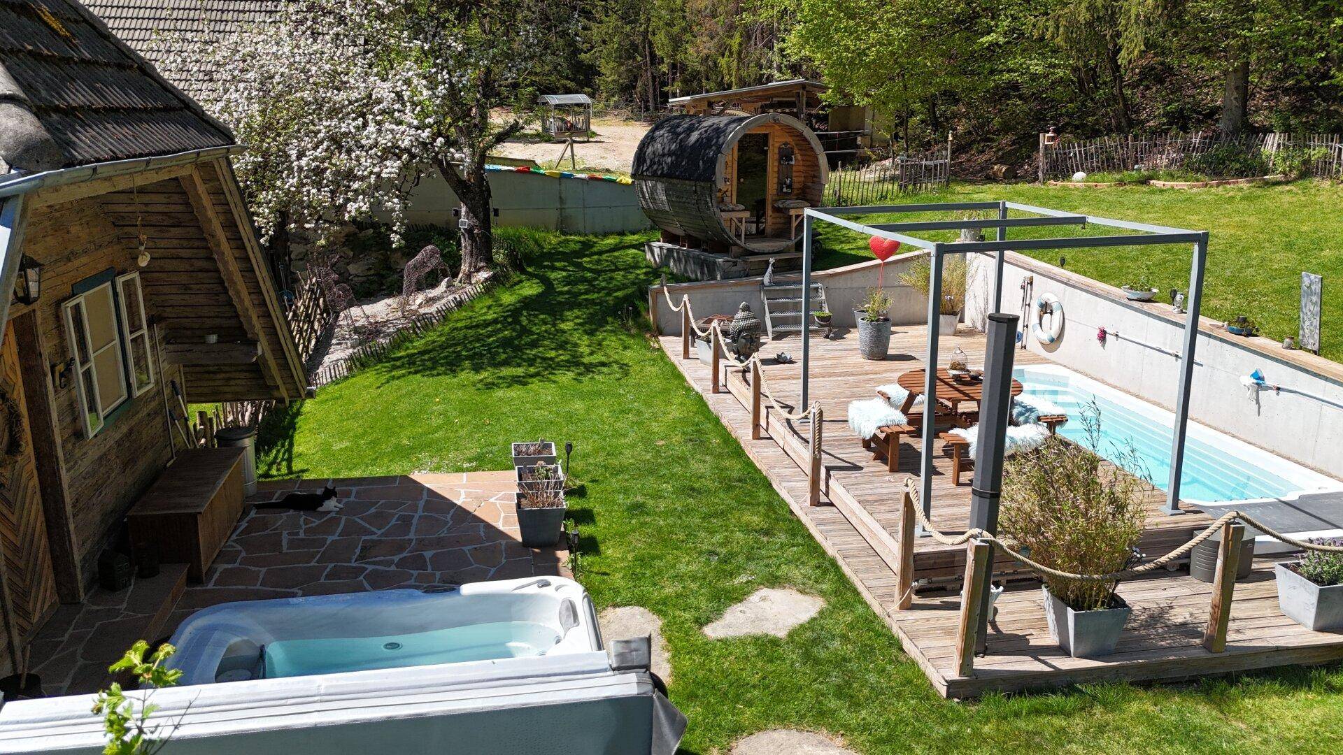 Großzügiger Gartenbereich mit Holzhaus, Whirlpool, Pool, Fasssauna und weitläufigen Rasenflächen.