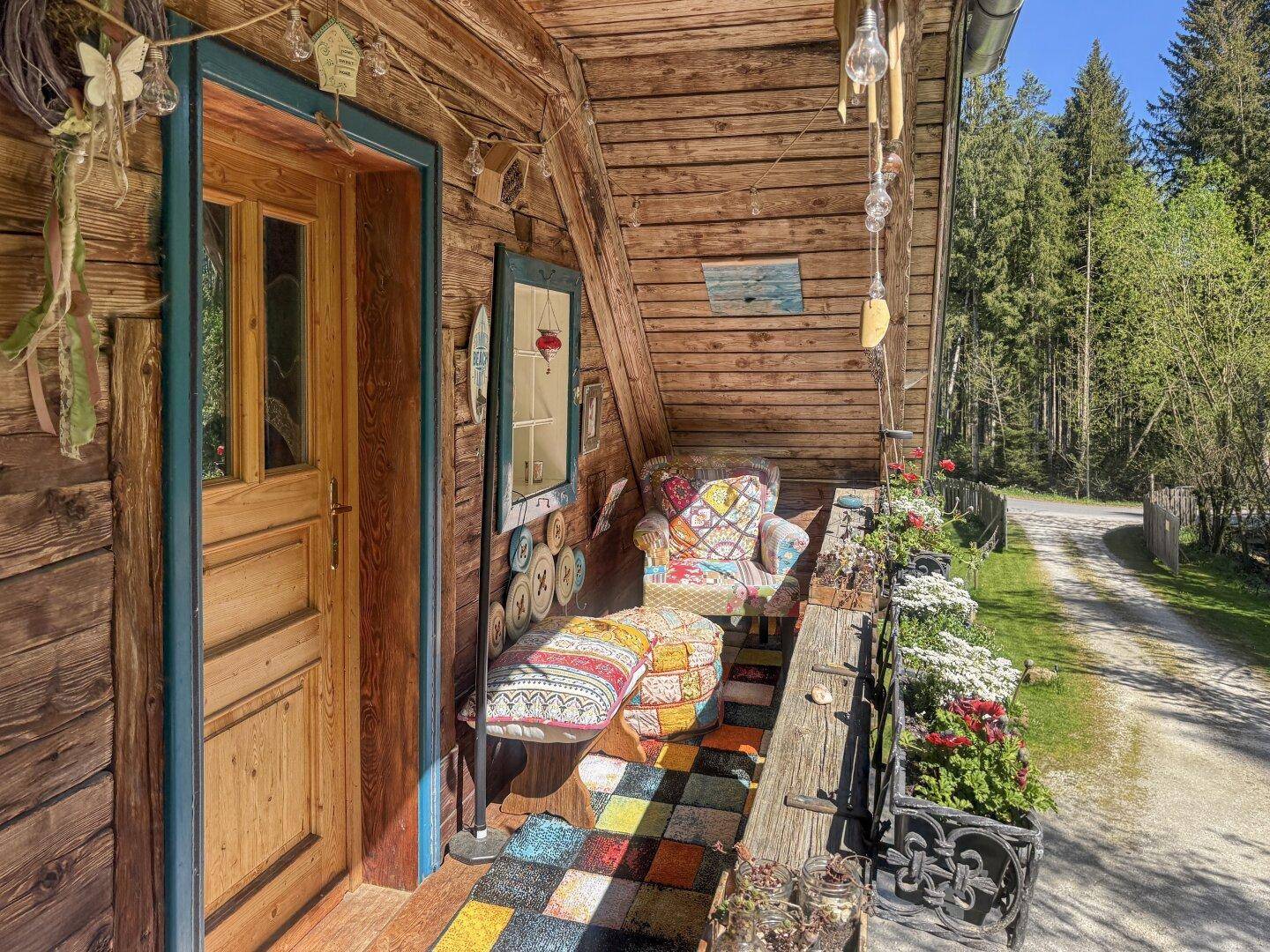 Gemütlicher Balkon mit Holzboden, bunten Kissen und Blick auf die grüne Umgebung.