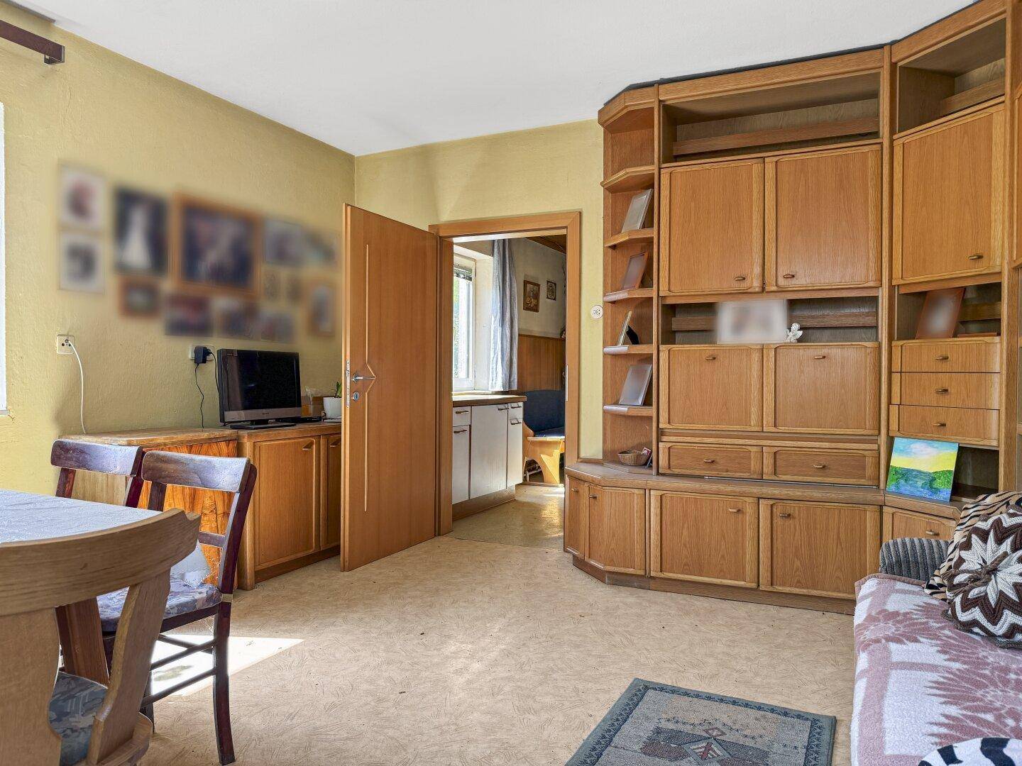 Geräumiges Wohnzimmer mit älteren Holzmöbeln und Blick in einen angrenzenden Raum.