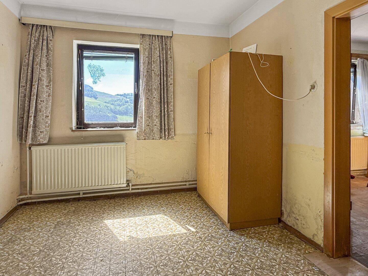 Einfaches Schlafzimmer mit Fensterblick ins Grüne und einem Kleiderschrank.