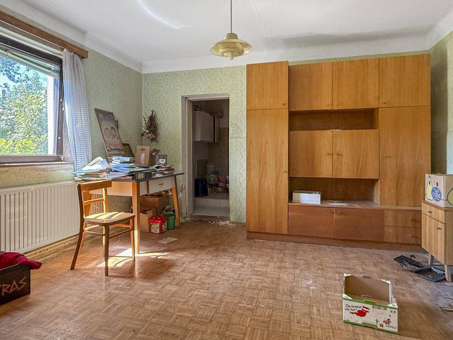 Wohnraum mit Holzmöbeln, Schreibtisch und Blick auf den Garten durch das Fenster.