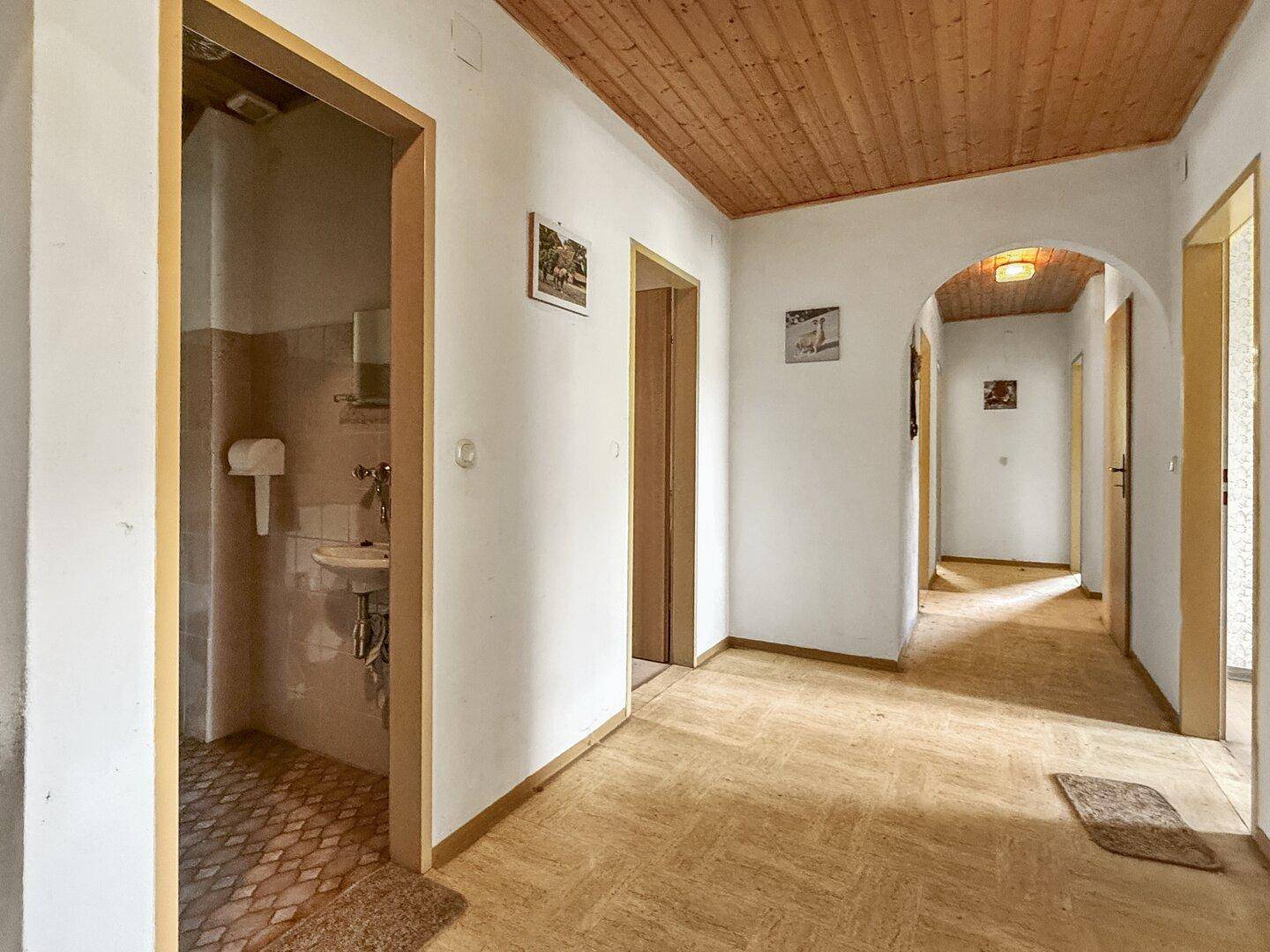 Flur mit Zugang zu einem kleinen Badezimmer mit Waschbecken und Fliesenboden.