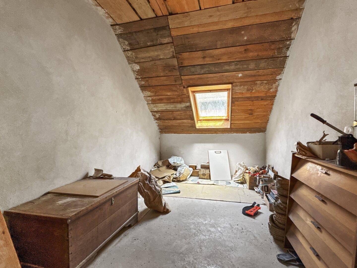 Unausgebauter Dachboden mit Holzbalken und einem Dachfenster, ideal als Abstellraum.