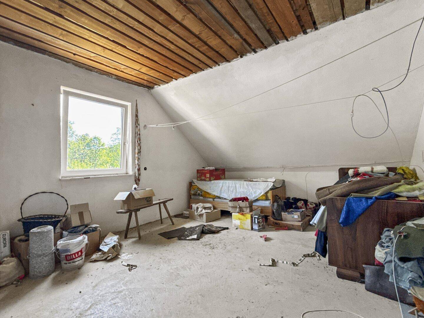 Geräumiger Dachboden mit Holzbalken und einem Fenster, das viel Tageslicht hereinlässt.