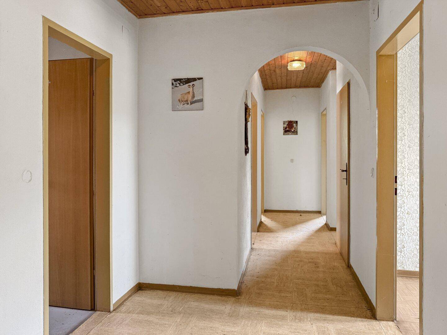 Flur mit Holzbalkendecke und einem Rundbogen, der zu weiteren Zimmern führt.