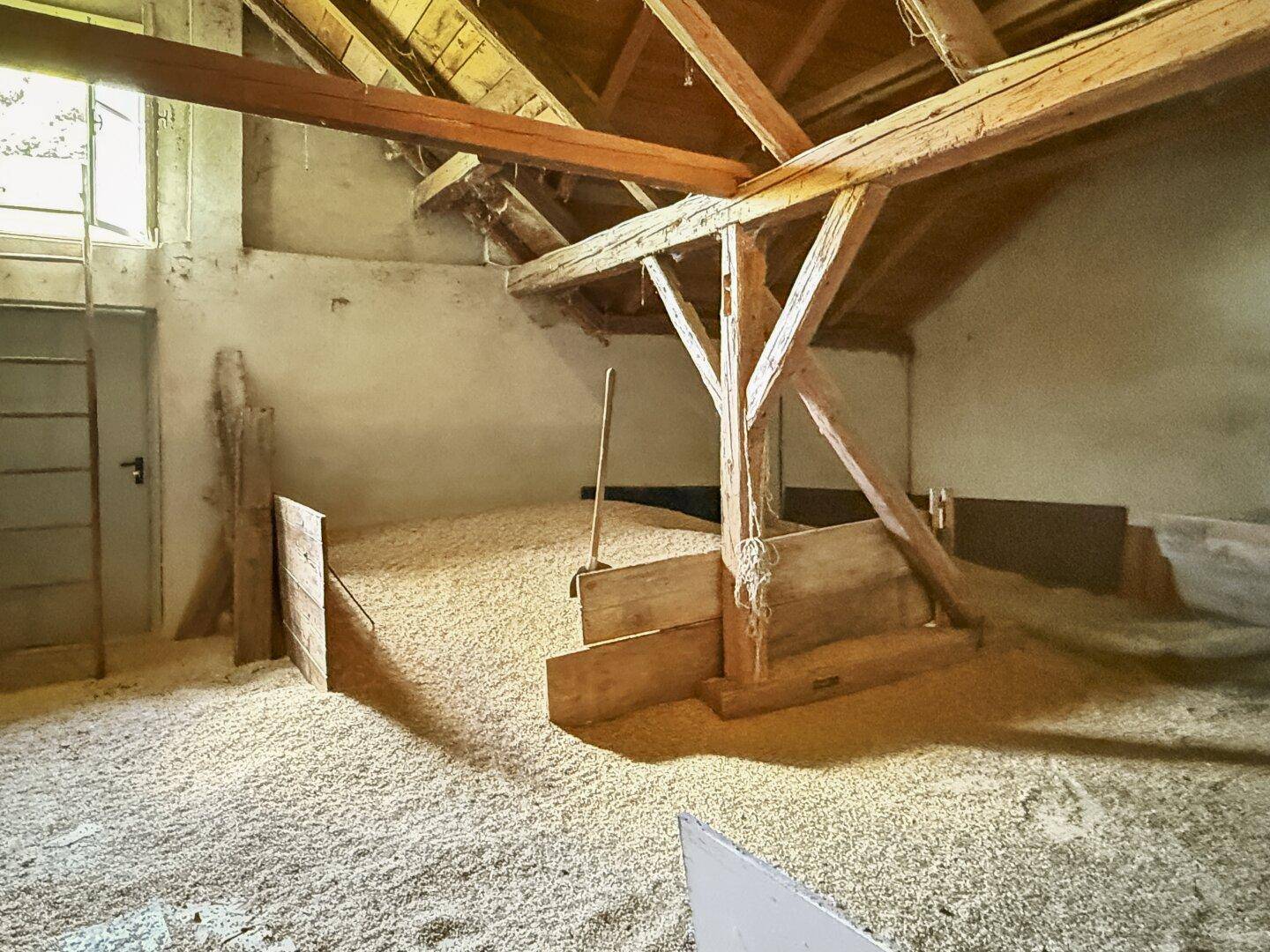Rustikaler Scheunenbereich mit Holzbalken und einer großen Menge Heu oder Stroh.