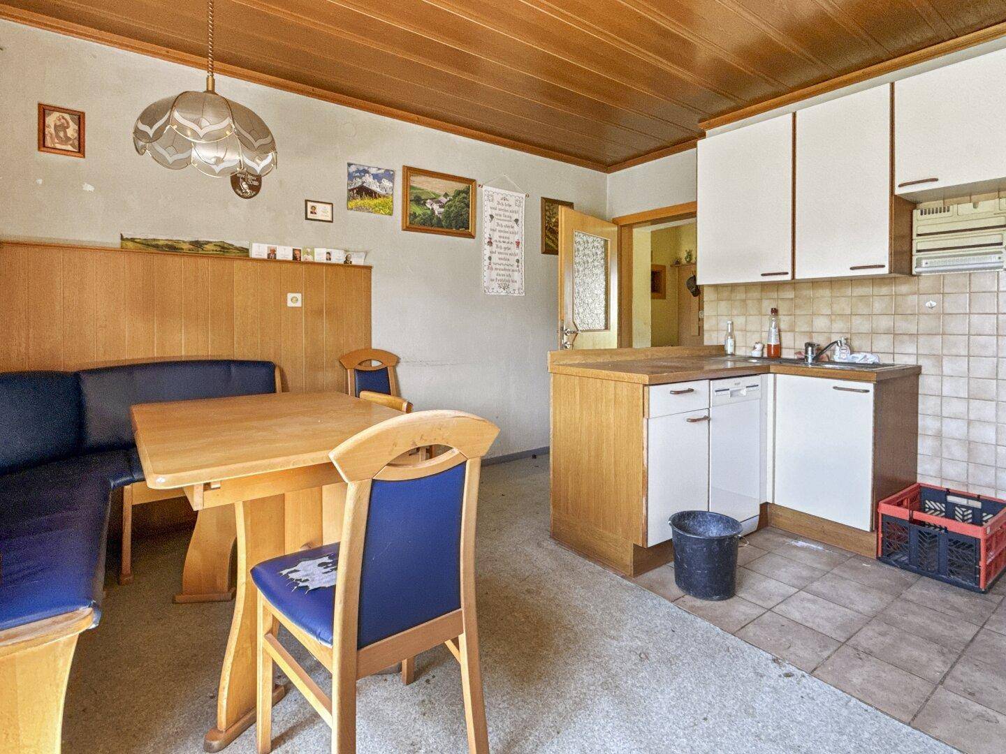 Wohnküche mit Holzvertäfelung an Decke und Wänden, Esstisch und einfachen Küchenschränken.