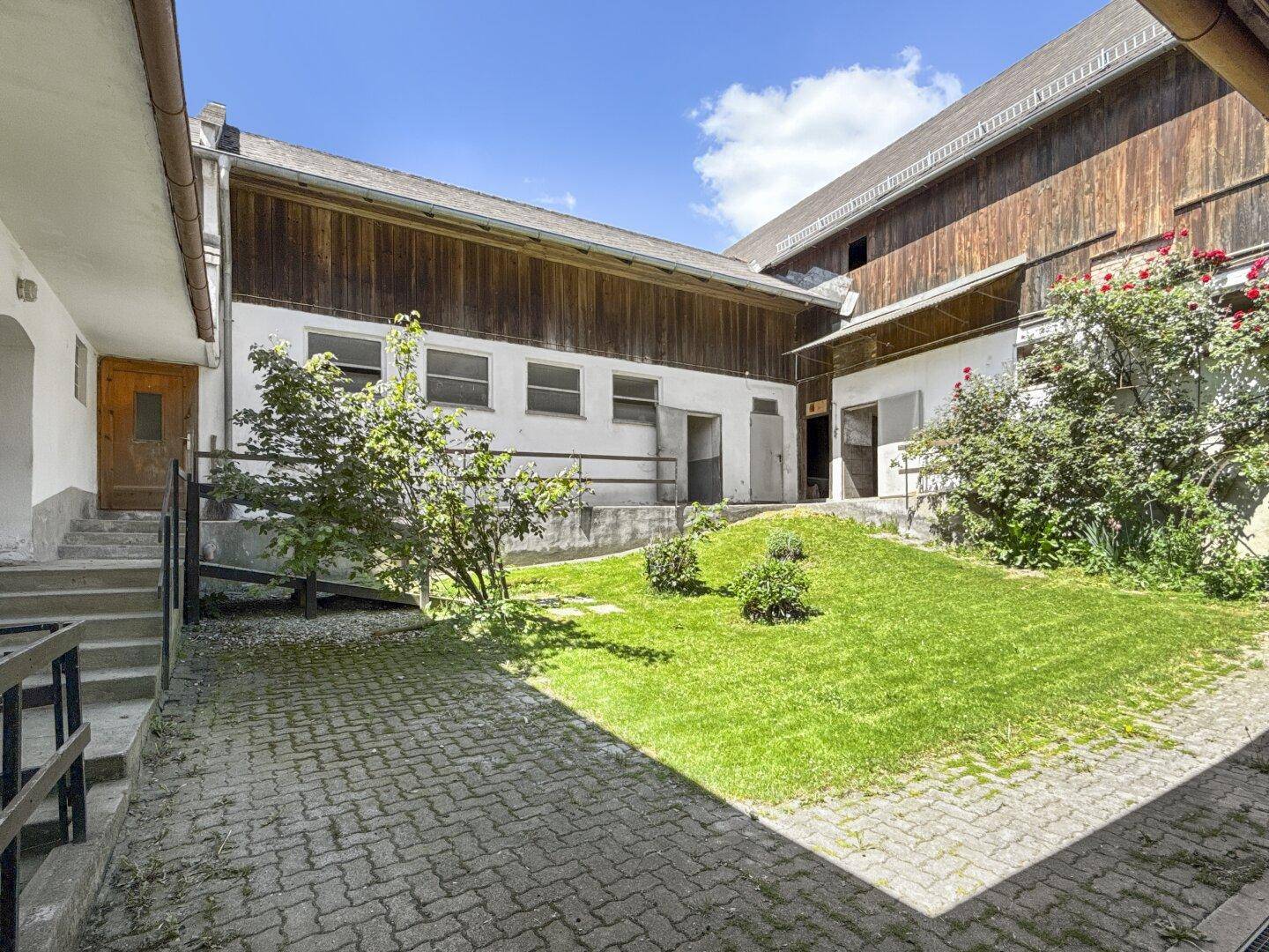 Innenhof mit gepflastertem Bereich, Rasenfläche und umgebenden Gebäuden.