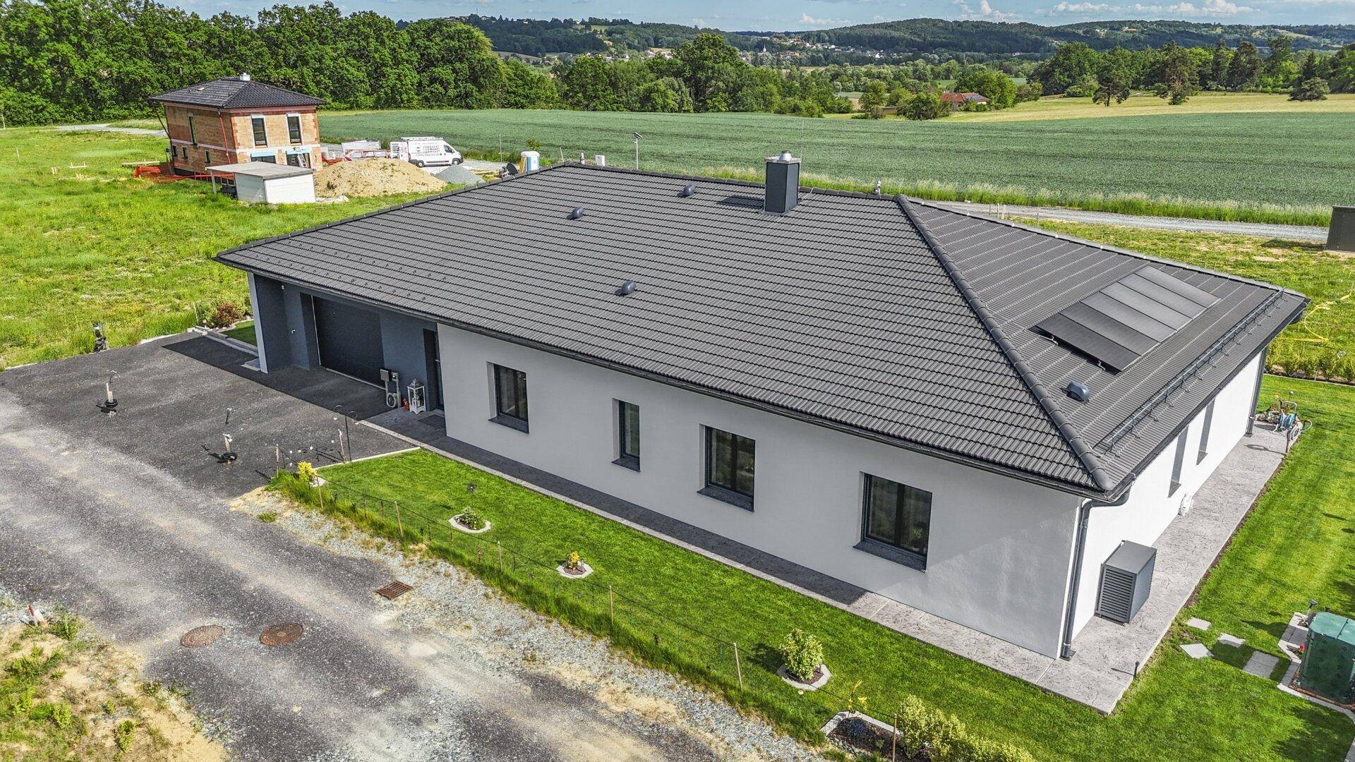 Luftaufnahme eines modernen Einfamilienhauses mit Satteldach, Photovoltaikanlage und weitläufiger Grünfläche.