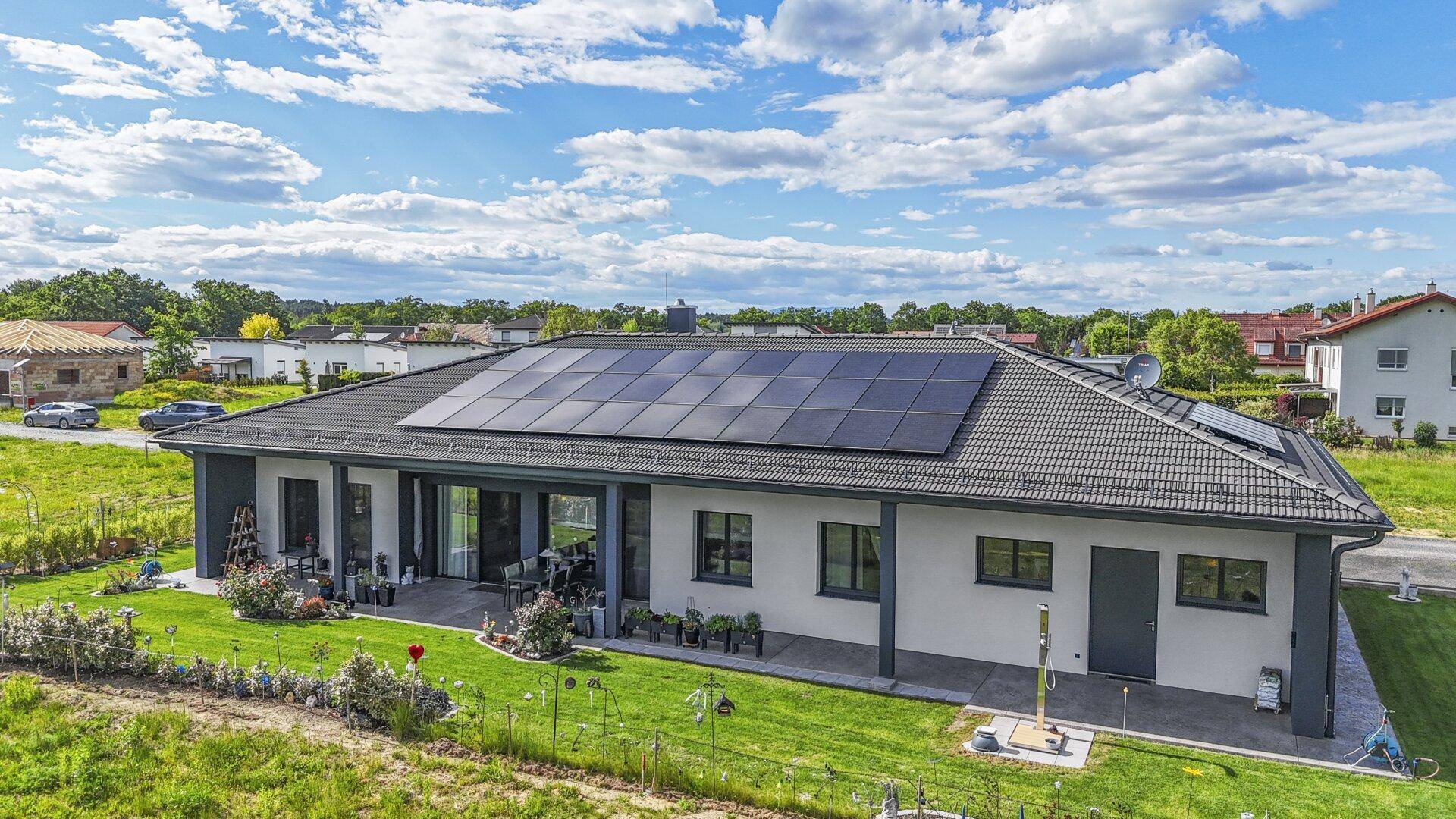 Rückseite des Hauses mit großer Terrasse, Gartenmöbeln, gepflegtem Rasen und Solaranlage auf dem Dach.