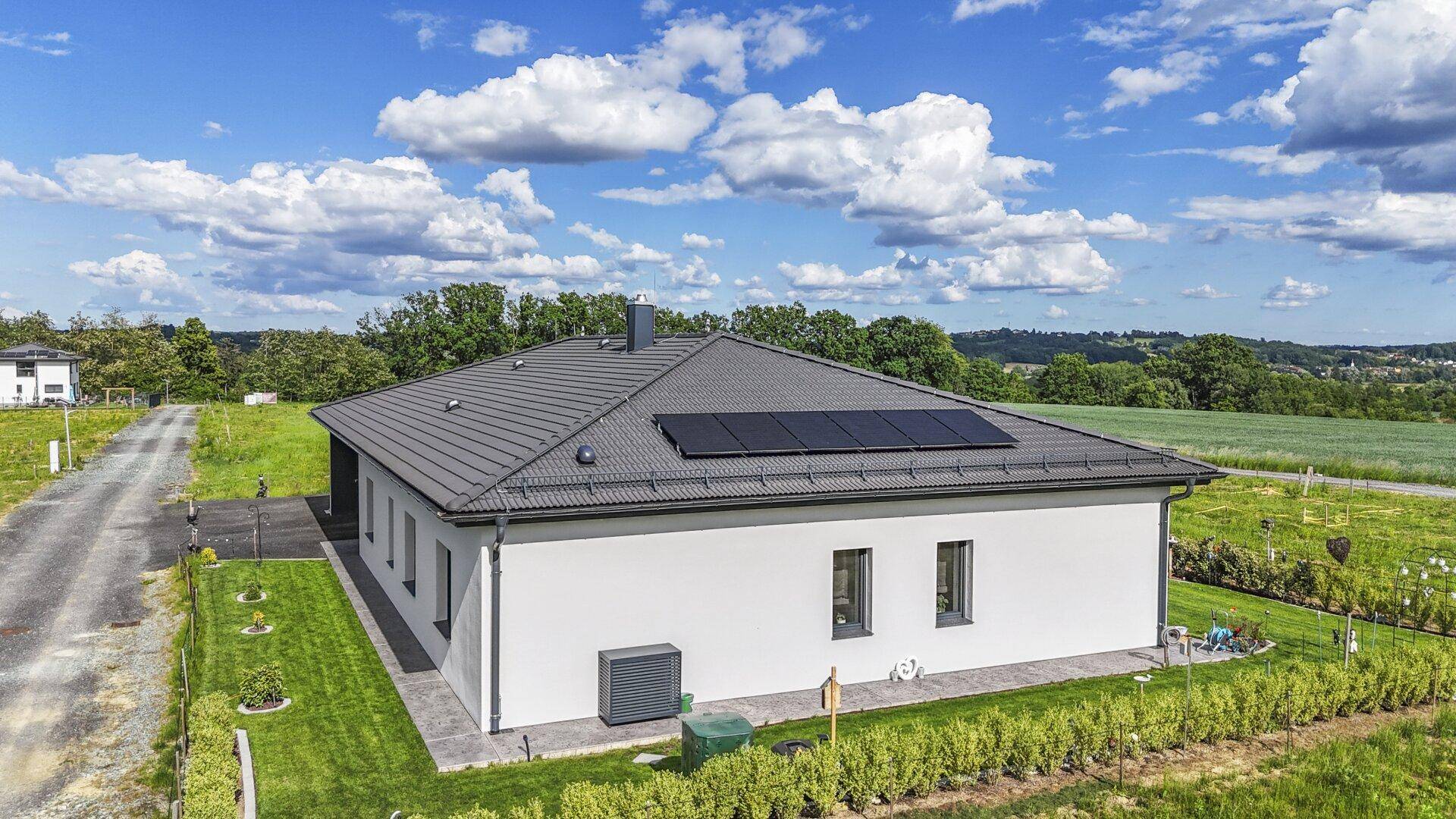 Seitenansicht des modernen Einfamilienhauses mit gepflegtem Rasen, Wärmepumpe und Solarmodulen auf dem Dach.