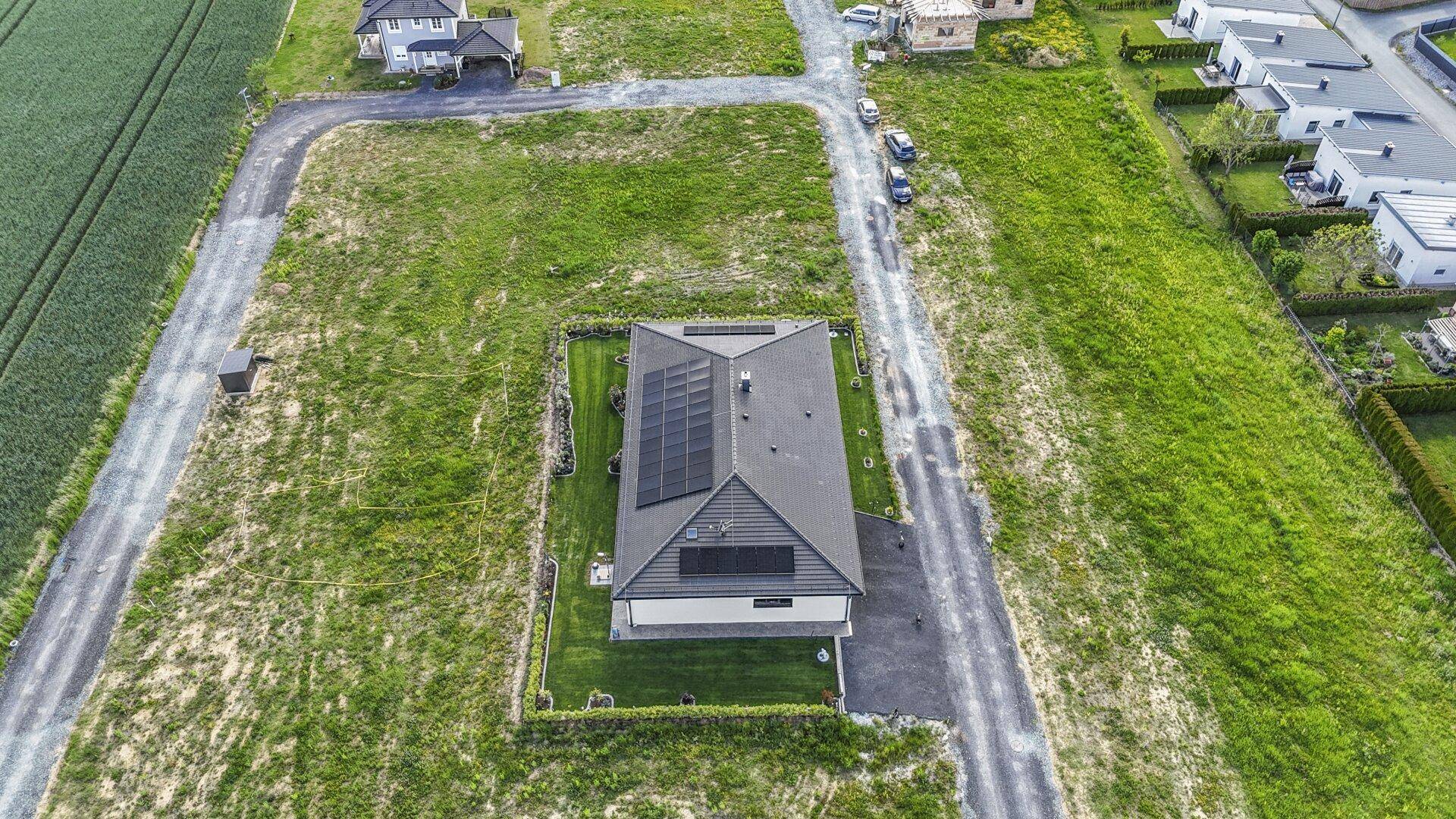 Gesamtansicht des Grundstücks von oben mit Einfamilienhaus, Photovoltaikanlage und umliegender Landschaft.