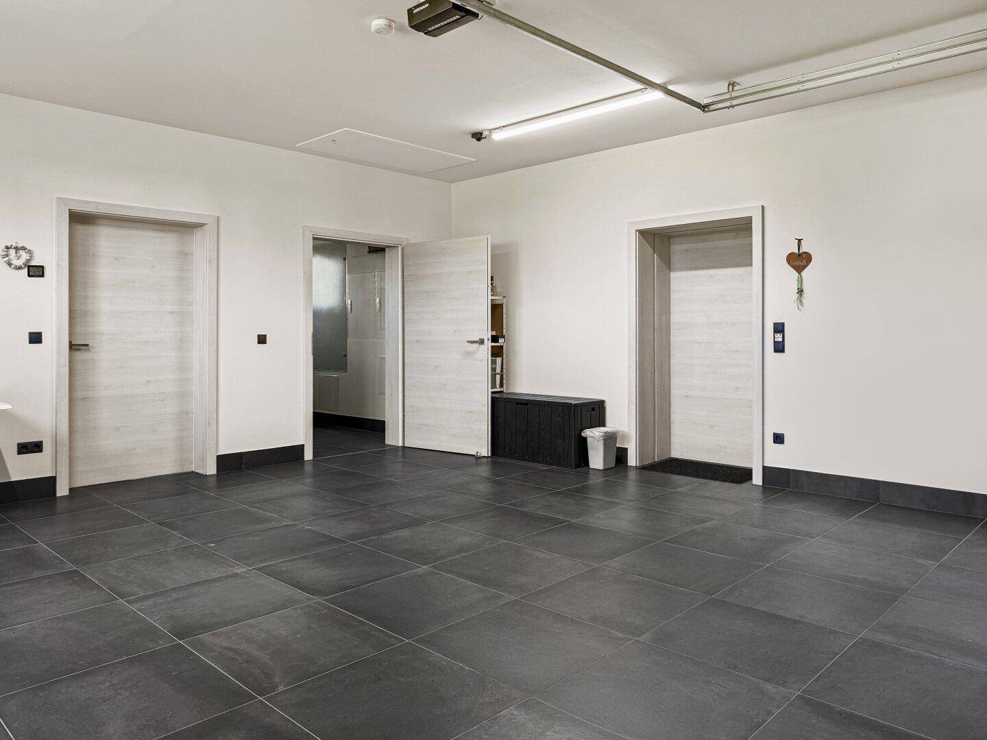 Heller Garageninnenraum mit drei Türen und robustem Fliesenboden, ideal für Fahrzeuge und Lagerung.